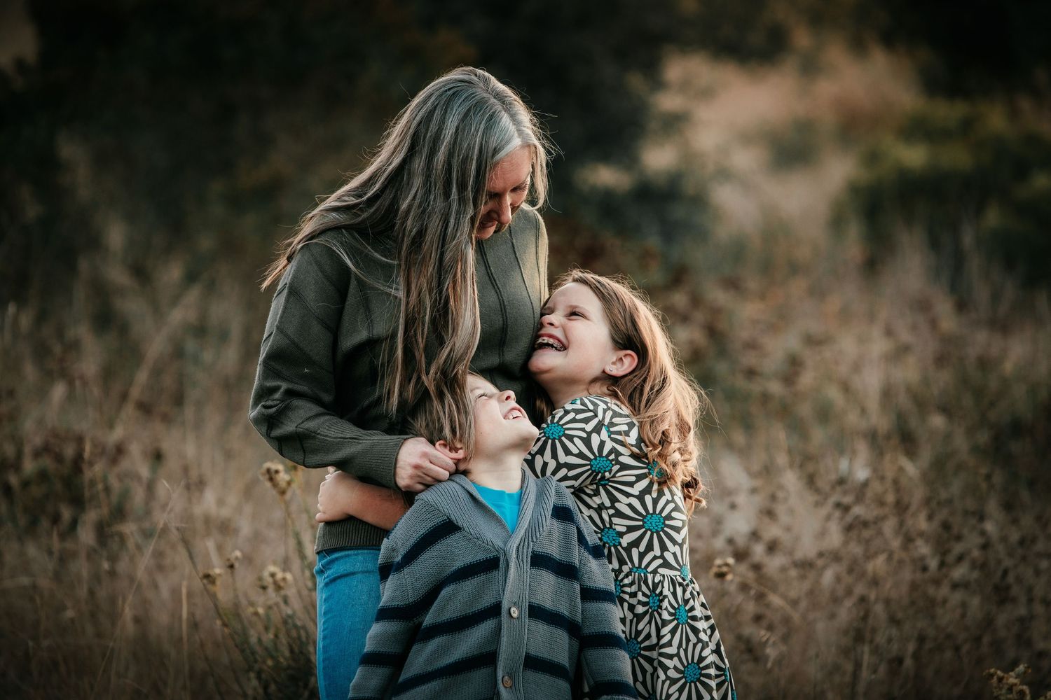 Grandmother laughing with two grandchildren in a golden field during an outdoor family portrait.