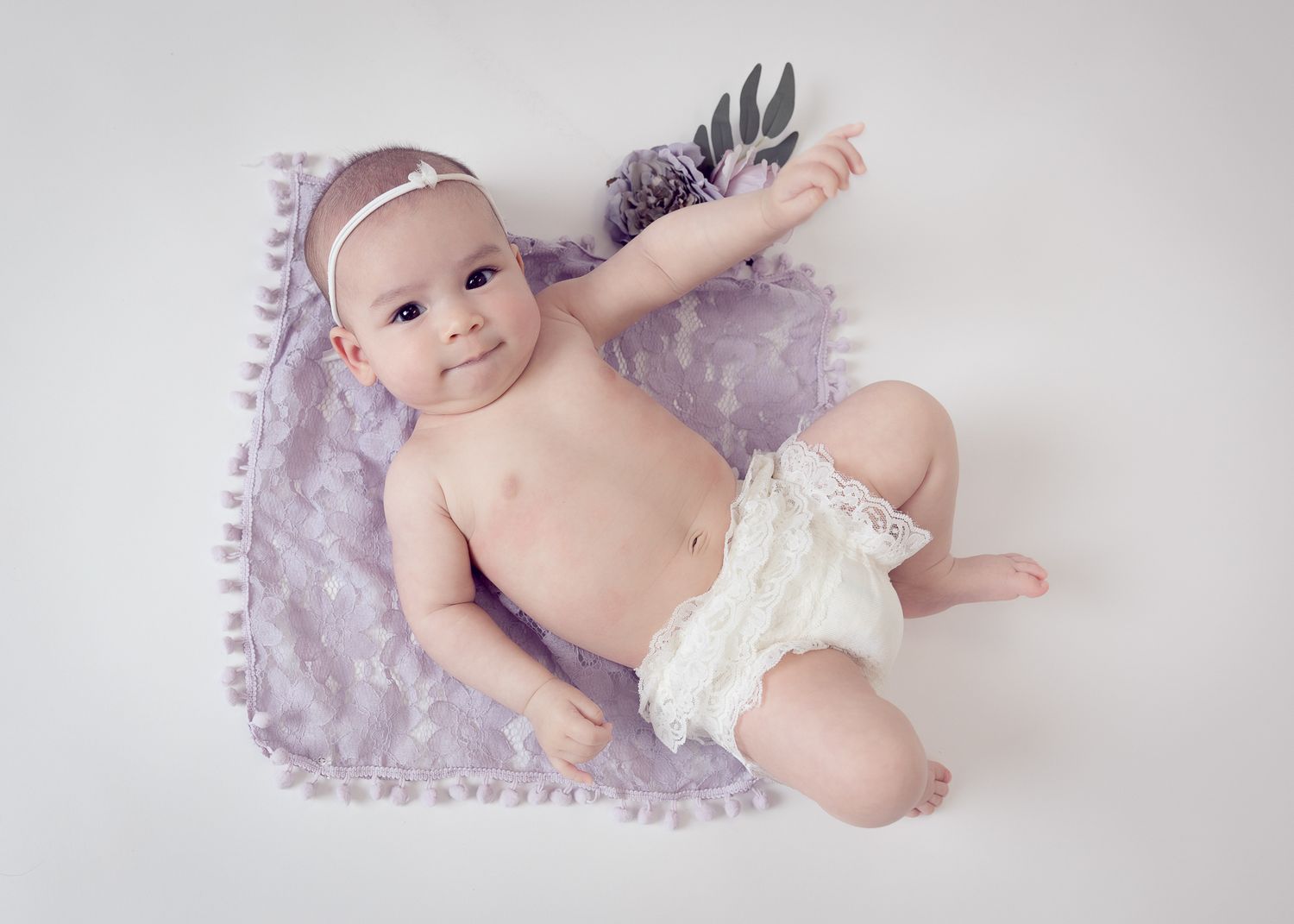 Cute baby in white lace bloomers on lavender blanket.