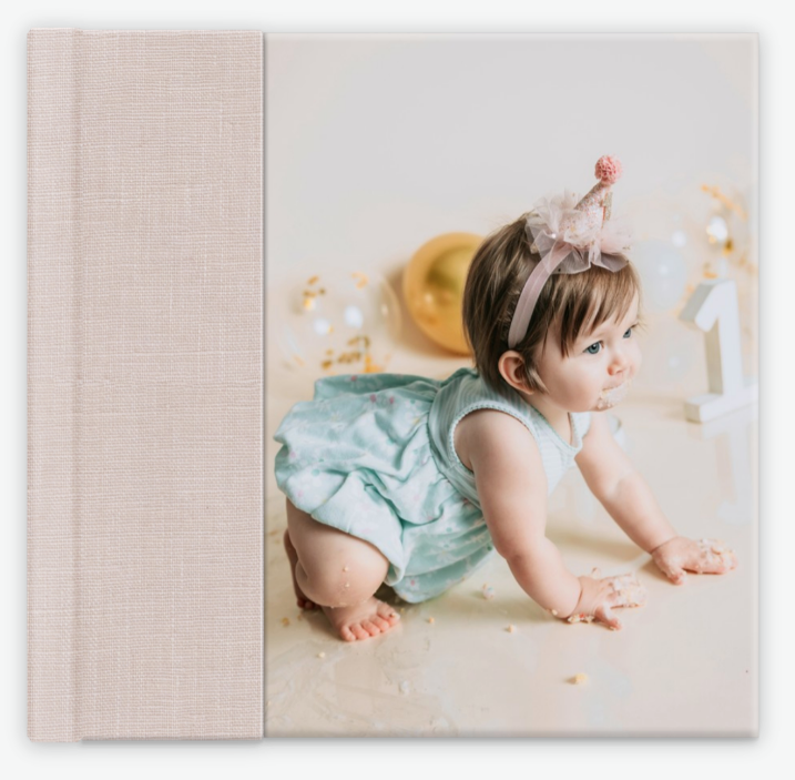 Square linen photo album with a cover image of a baby girl in a teal outfit during a first birthday session. Vista Newborn Photographer