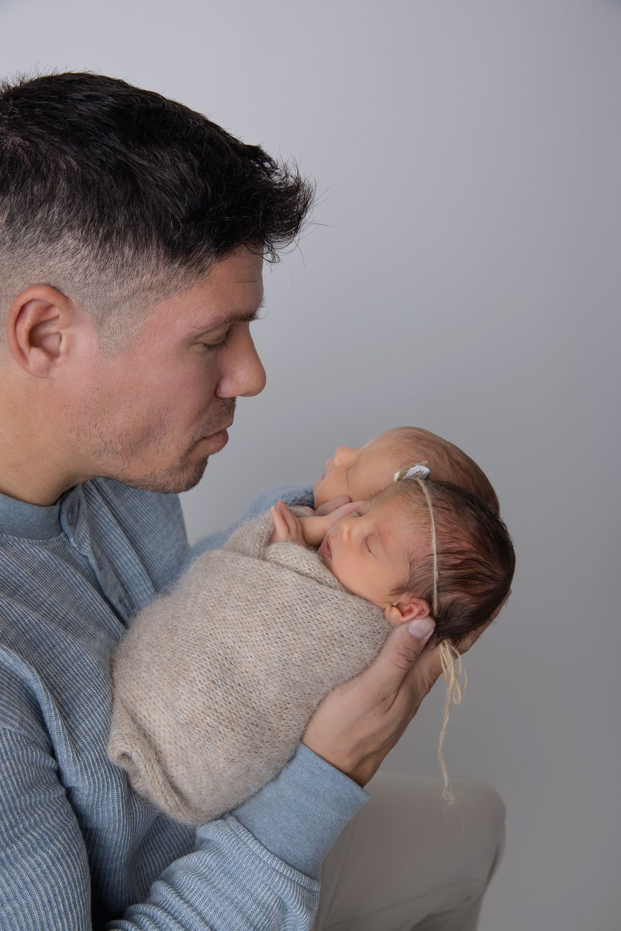 Loving father gently holding swaddled newborn baby close to his face against a neutral background at The Studio Bonsall, near Fallbrook