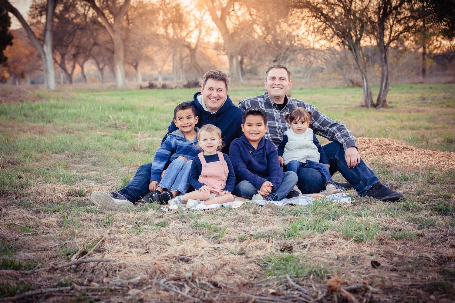 Two dads with four children sitting on blanket in golden sunset field in Bonsall CA