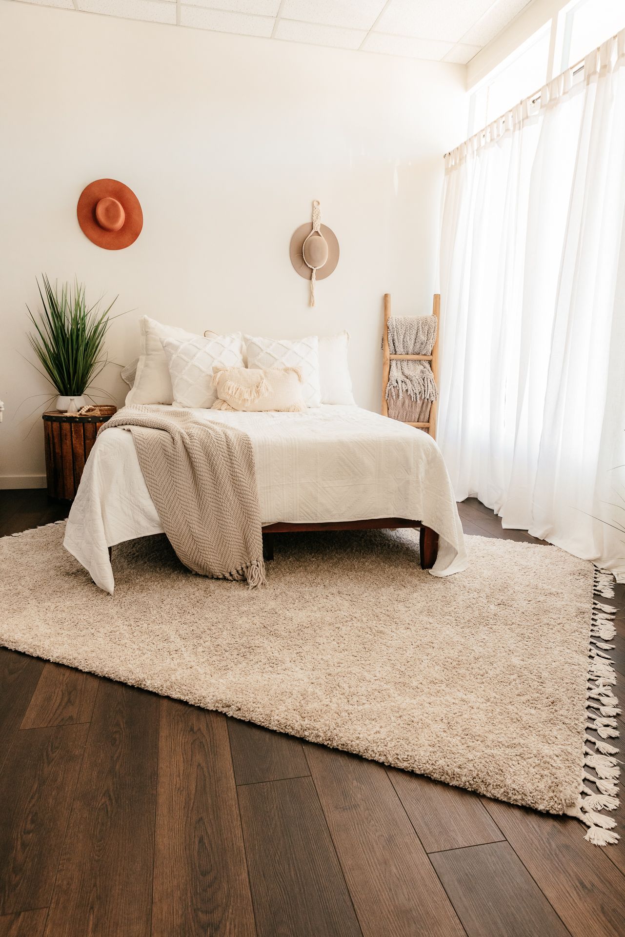 Boho bedroom with white bed, shag rug, wooden ladder, sheer curtains, and straw hat wall accents. in the Bonsall Studio near Fallbrook, Vist