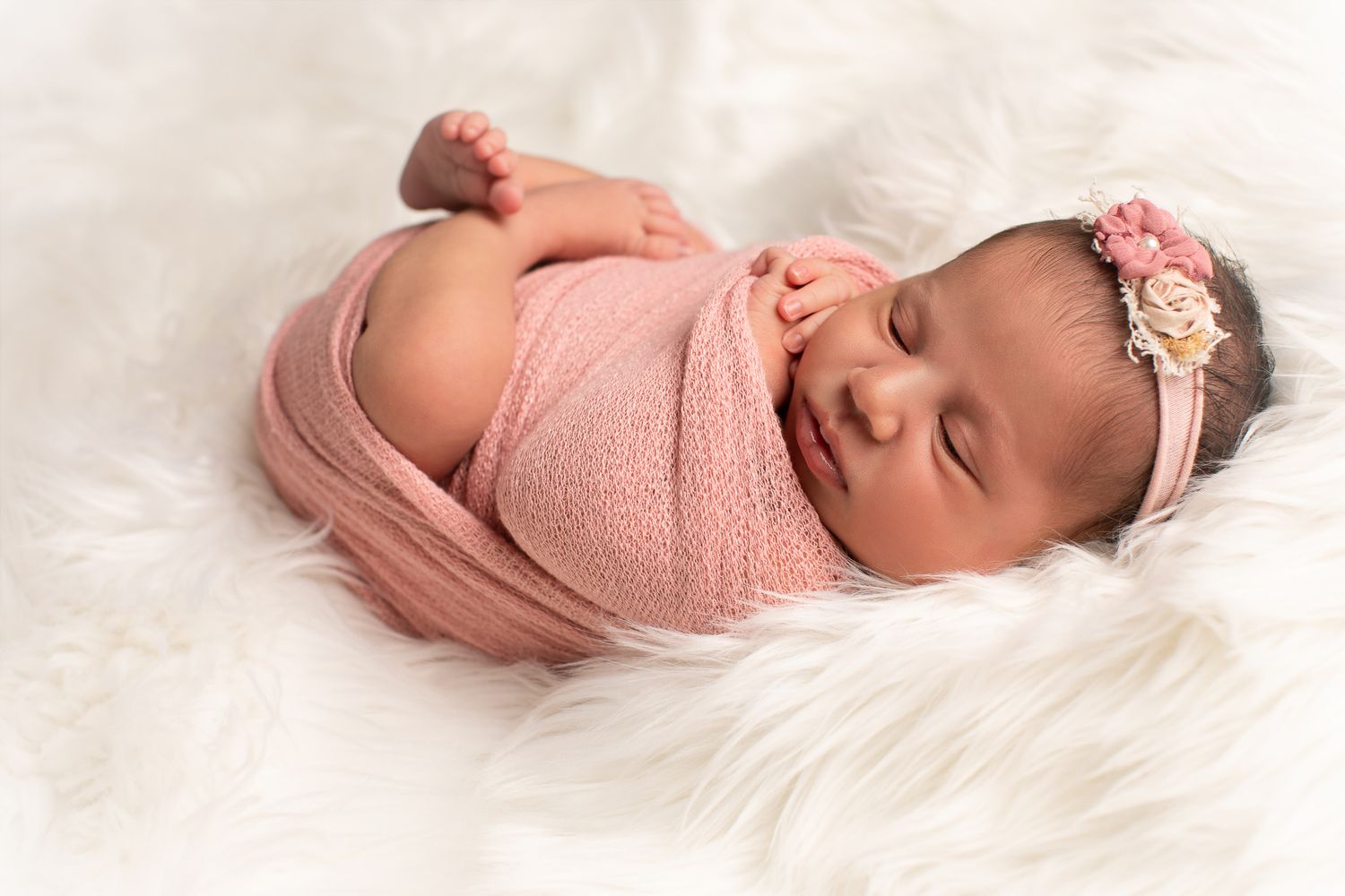 Newborn baby wrapped in pink swaddle with floral headband sleeping on white fluffy blanket at The Studio Bonsall, near Camp Pendleton Oceans