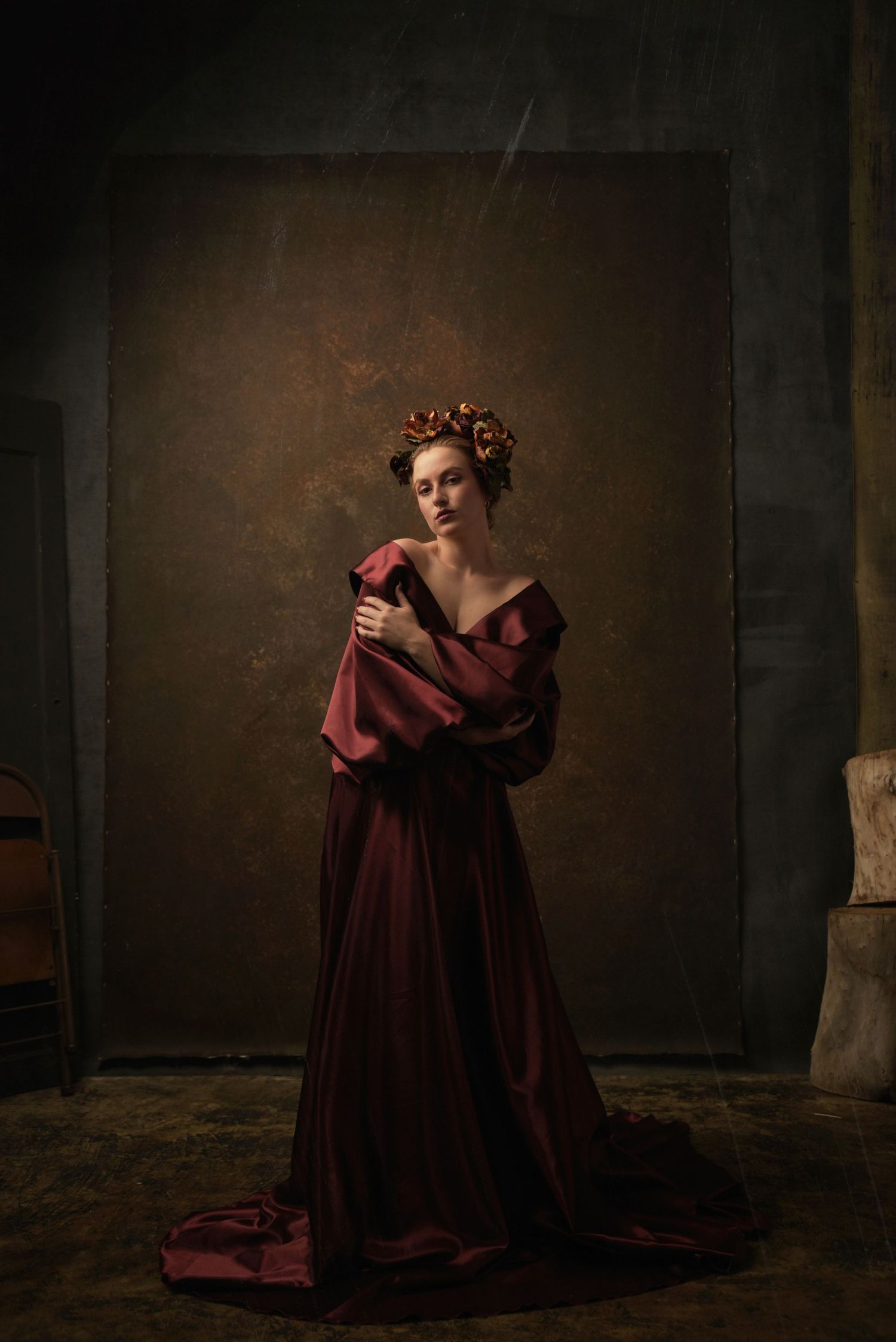 Dramatic pose in flowing burgundy gown with Renaissance styling against dark background.
