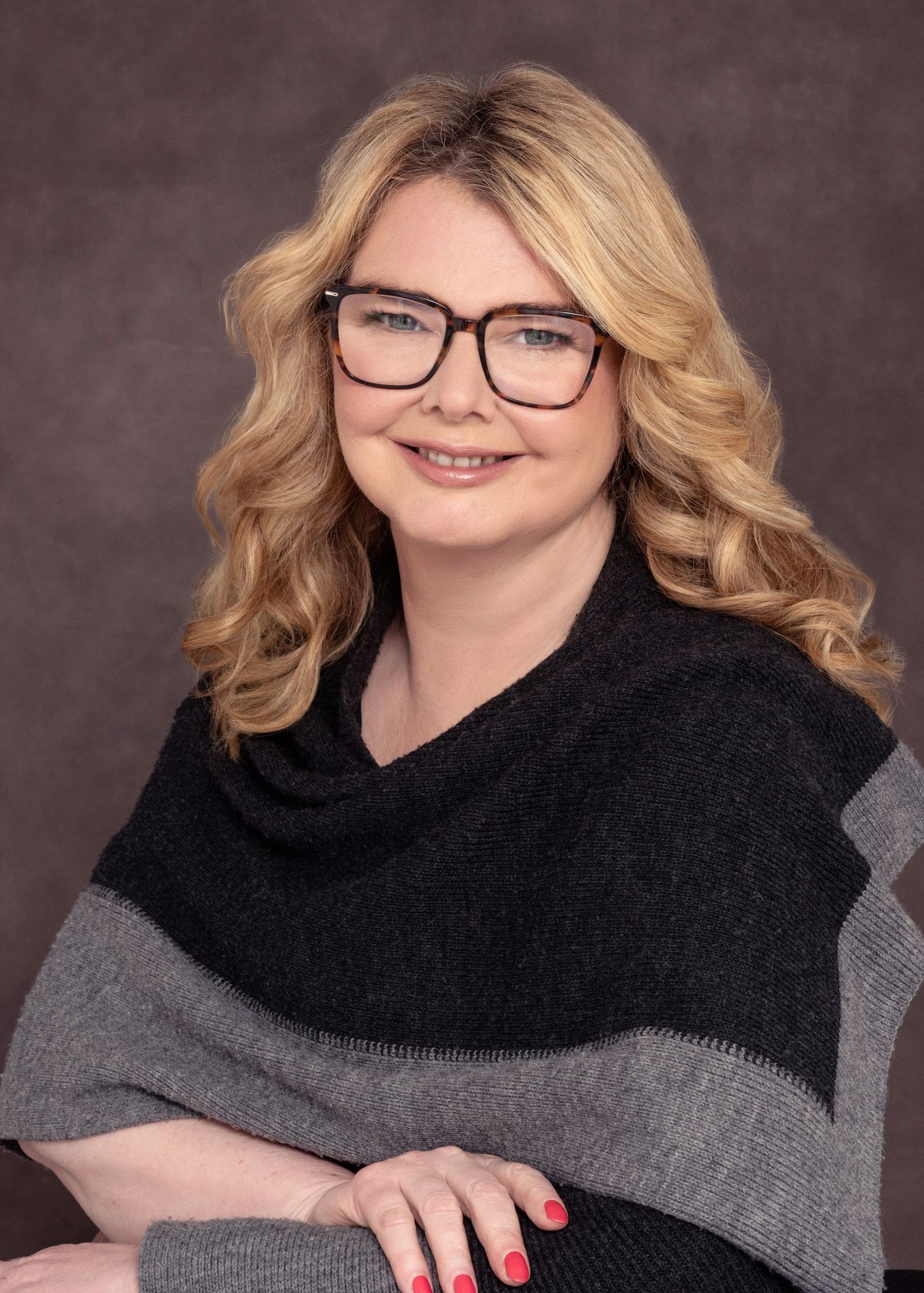Professional studio portrait in black sweater with modern glasses and wavy hair.