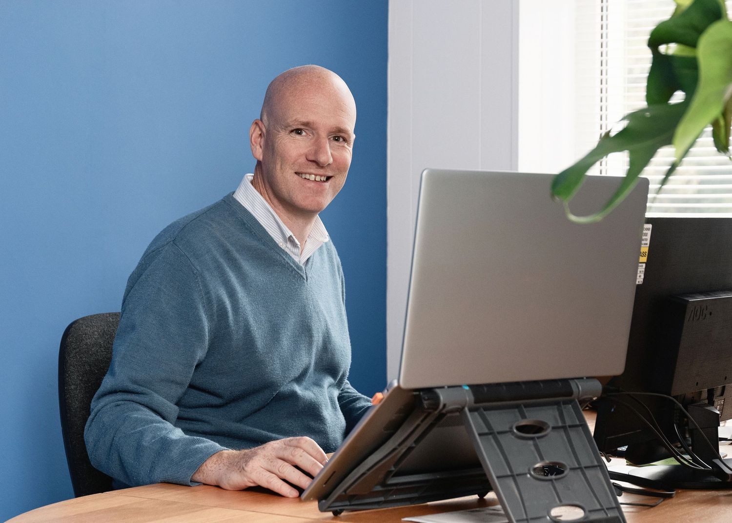 Professional in business attire working at desk with multiple computer monitors in modern office setting.