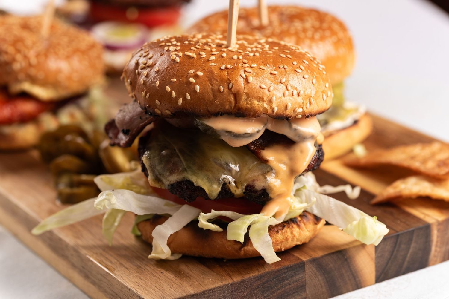 Juicy double cheeseburger with melted cheese, lettuce, and toppings on a sesame bun, served on a wooden board.