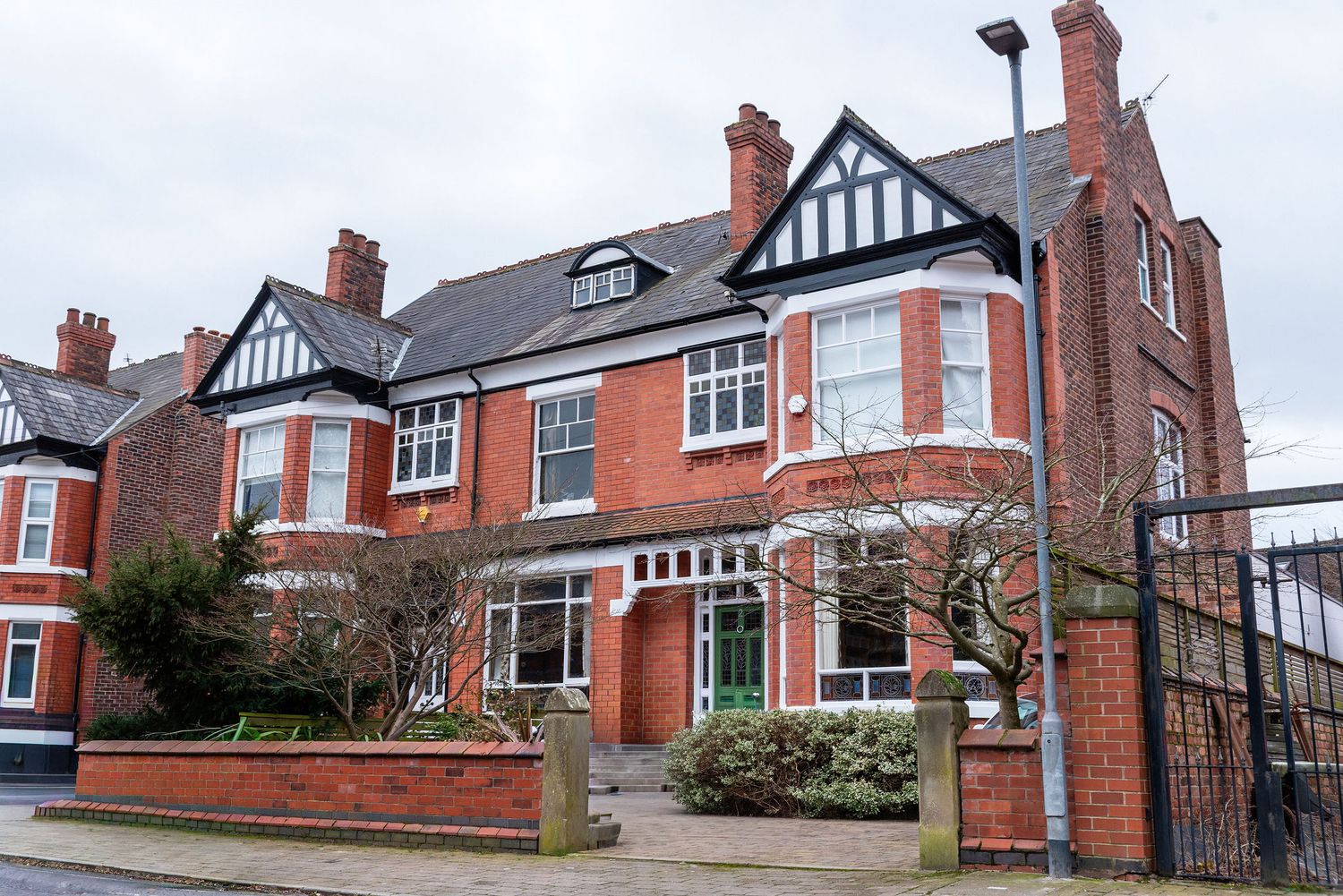 Row of traditional red brick Tudor-style houses with gabled roofs and chimneys along a residential street.