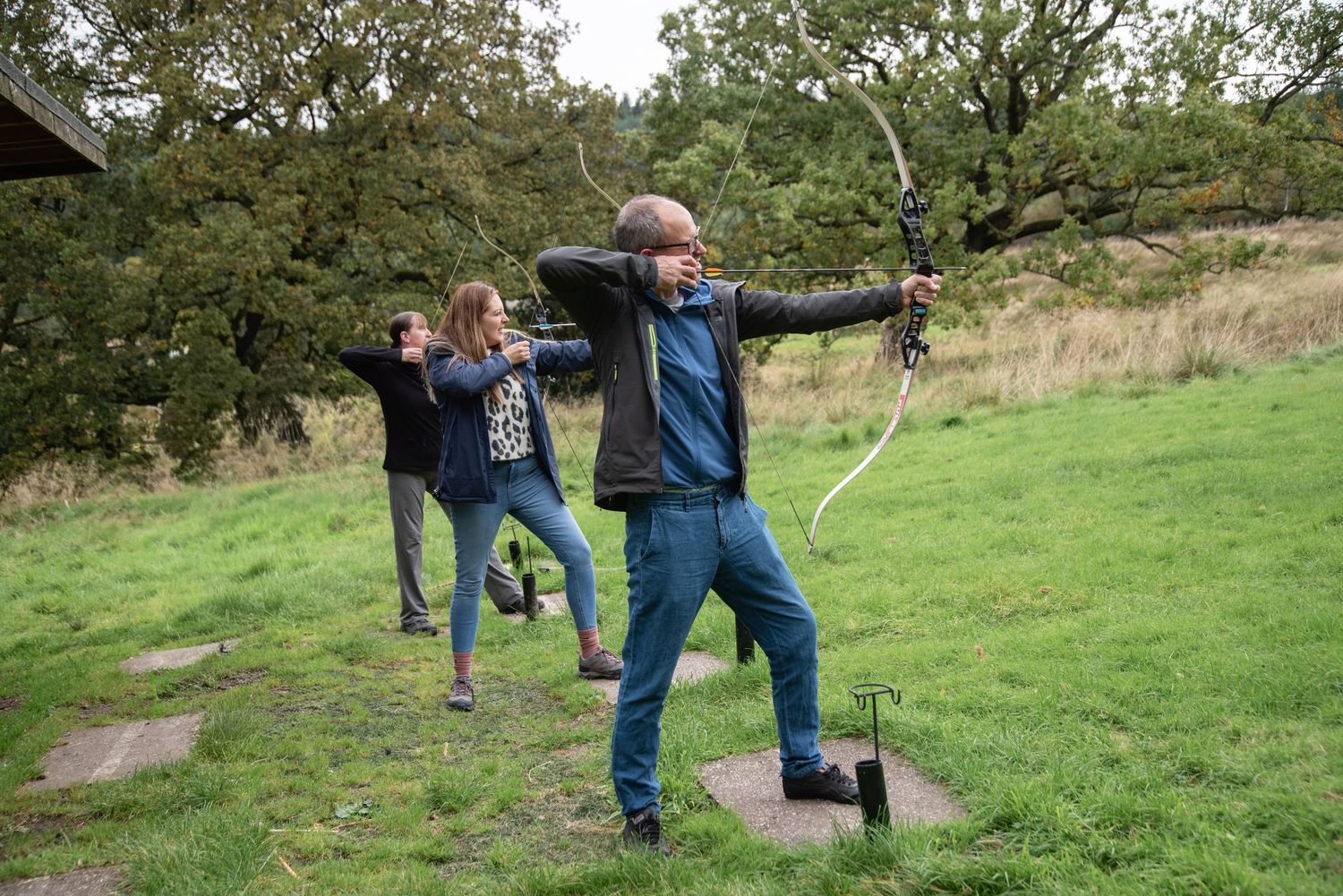 Groups of archers practice traditional archery technique with longbows in an outdoor field setting.