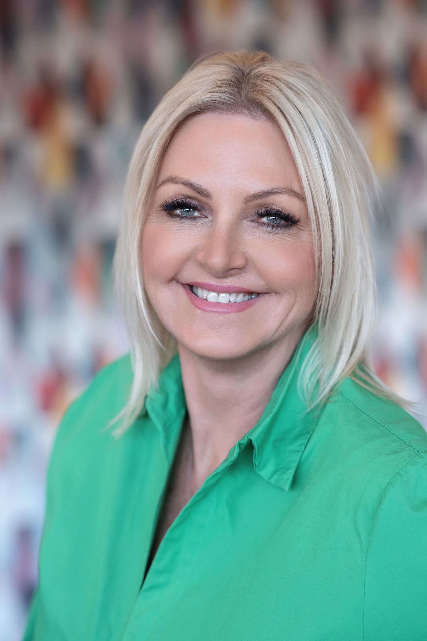 Professional portrait of a person wearing a bright green button-up shirt against a blurred colorful background.