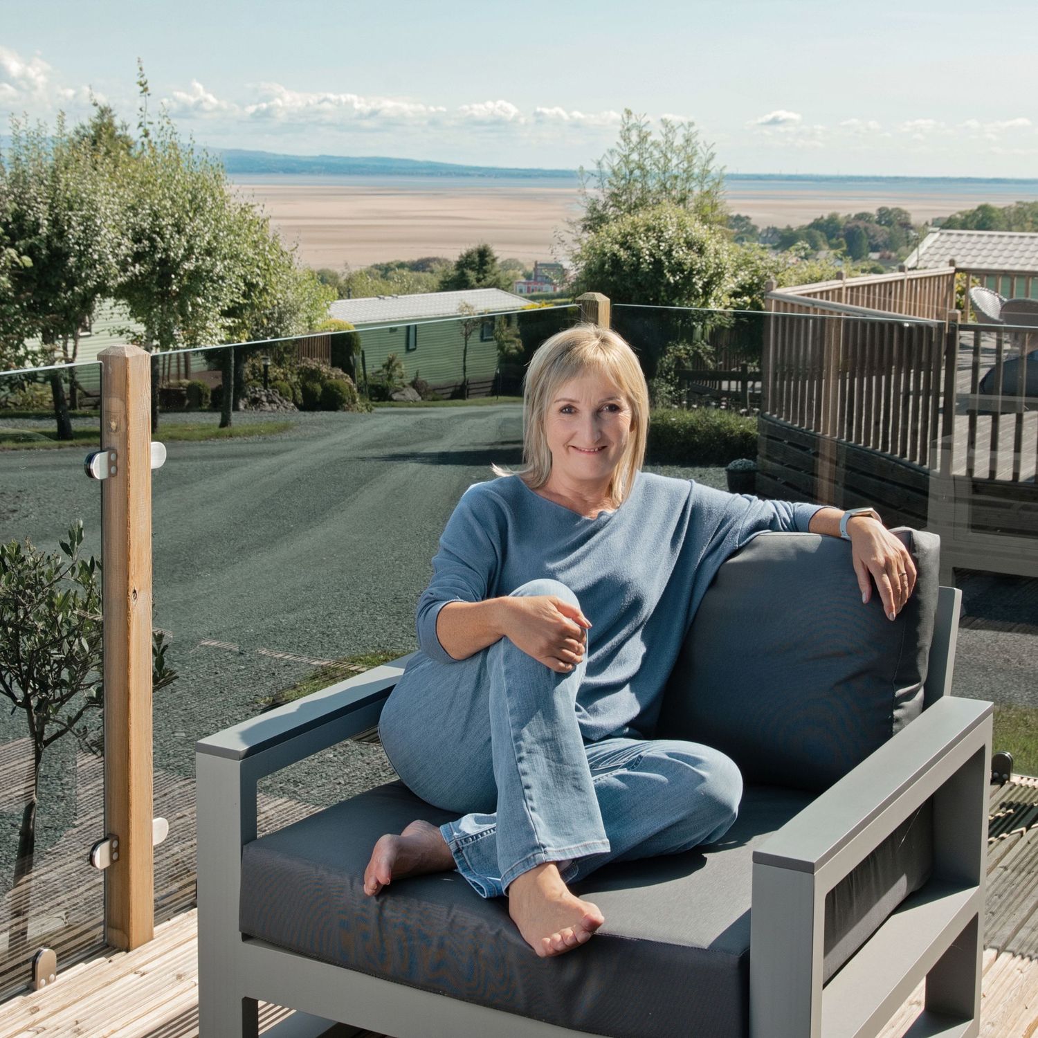 Woman relaxing on modern outdoor sofa on deck with scenic coastal views and blue sky backdrop.