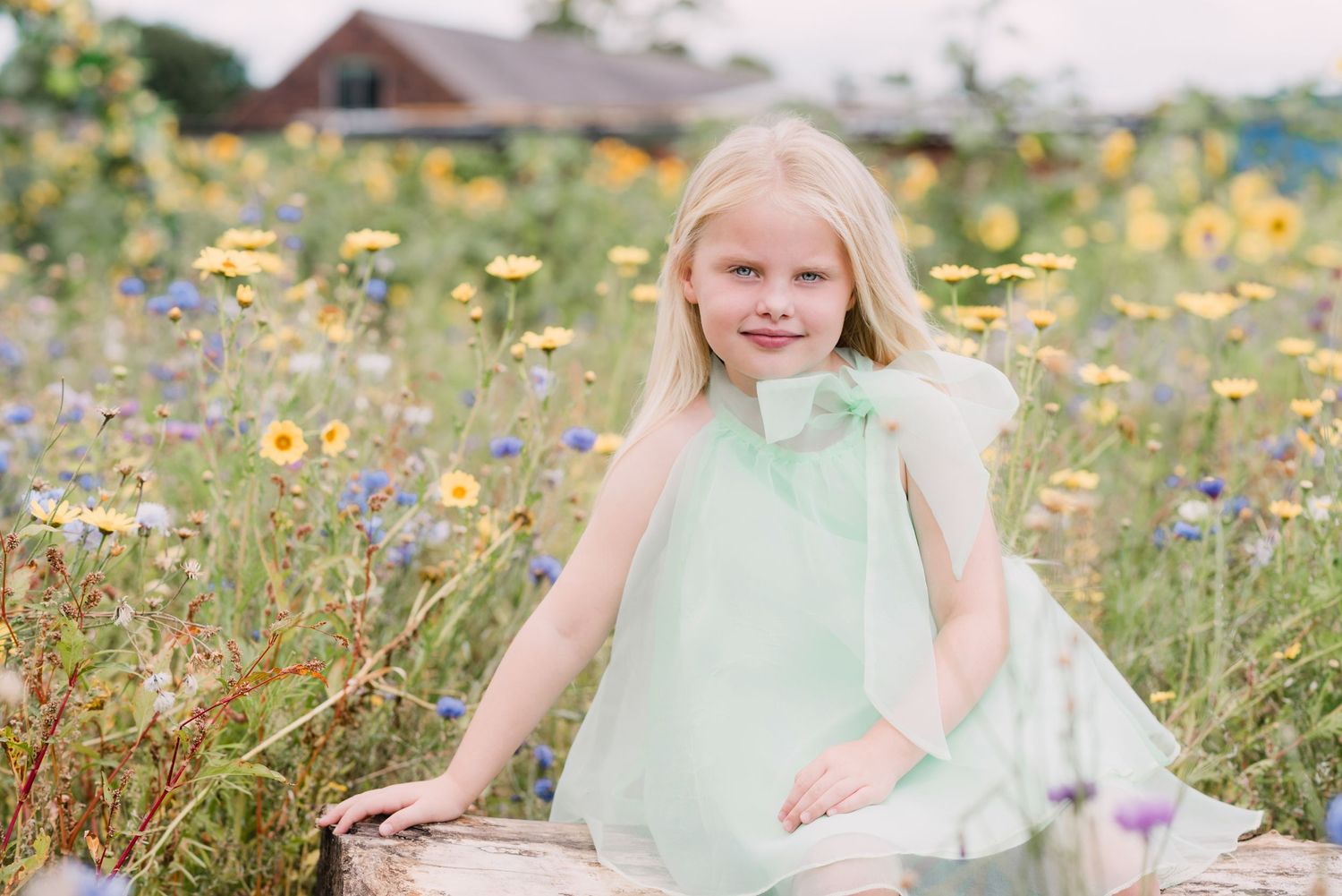Blonde girl in mint dress sitting among colorful wildflowers in a sunny meadow.