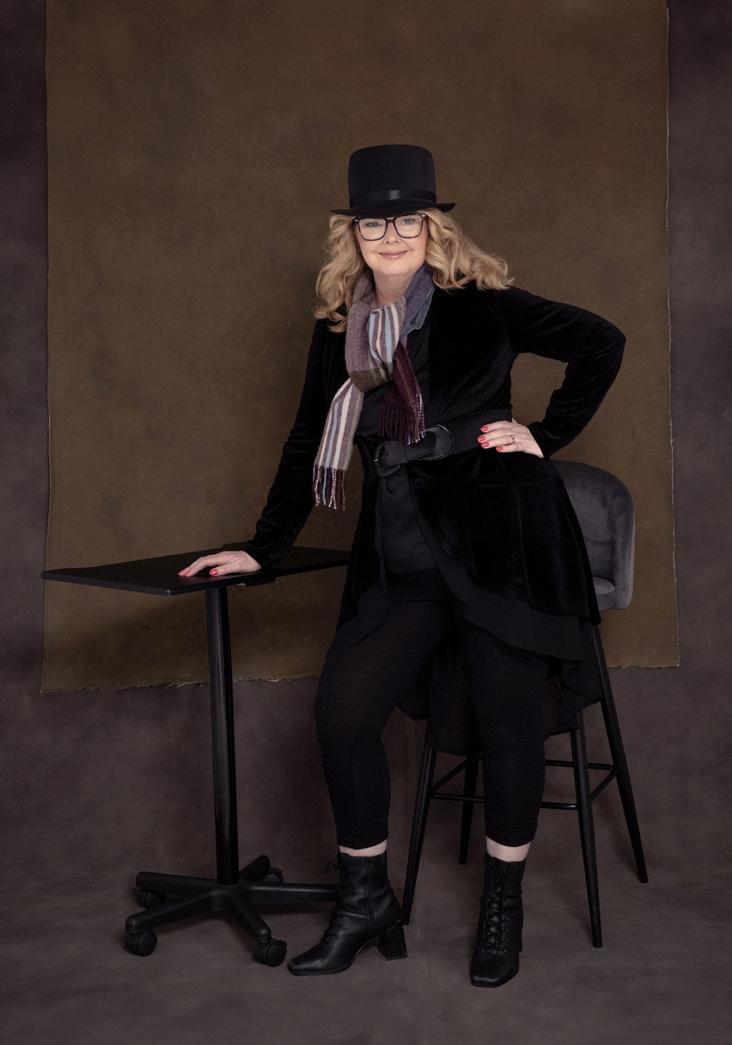 Stylish portrait with black top hat, velvet coat and boots in studio setting.