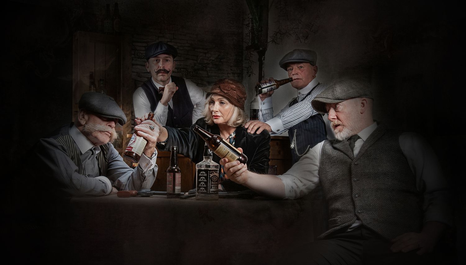 Dark moody scene of people in period clothing playing cards around a dimly lit table.