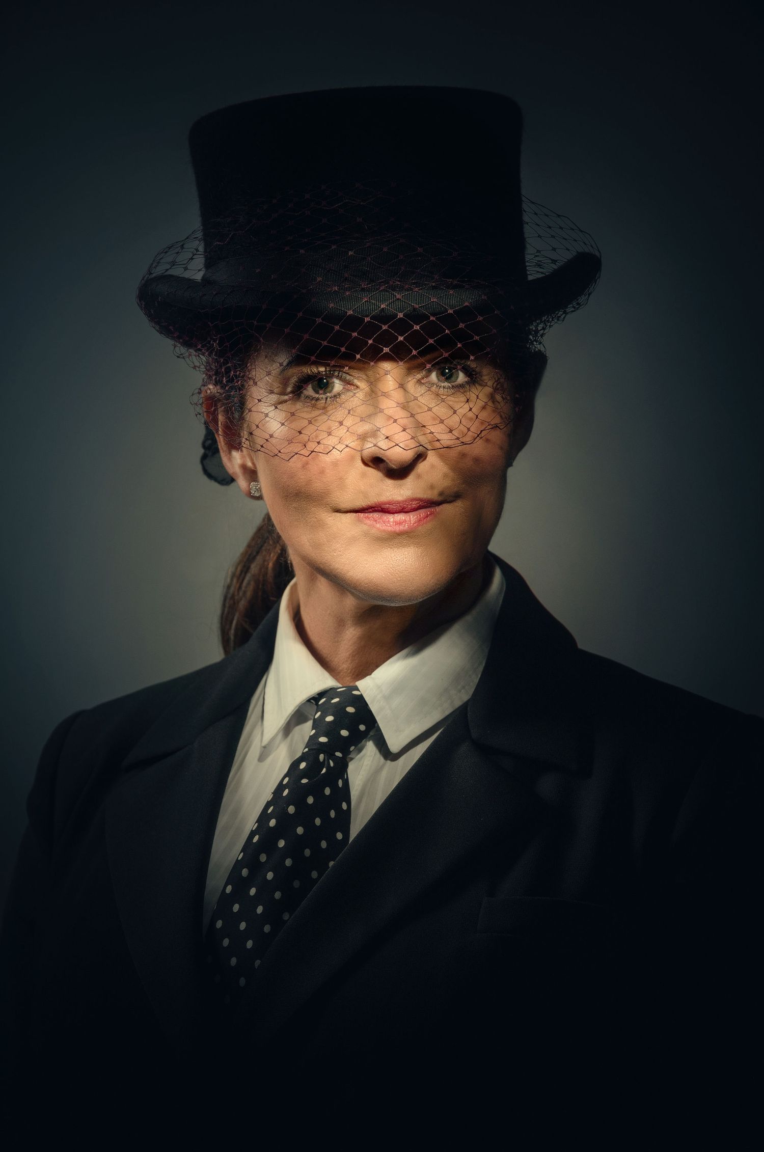 Dramatic portrait showing vintage style with top hat and veil against dark background.