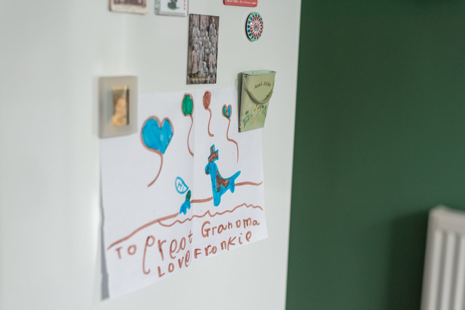 Child's drawing on white paper posted on a fridge, addressed to Grandma with love, featuring colorful balloon artwork.
