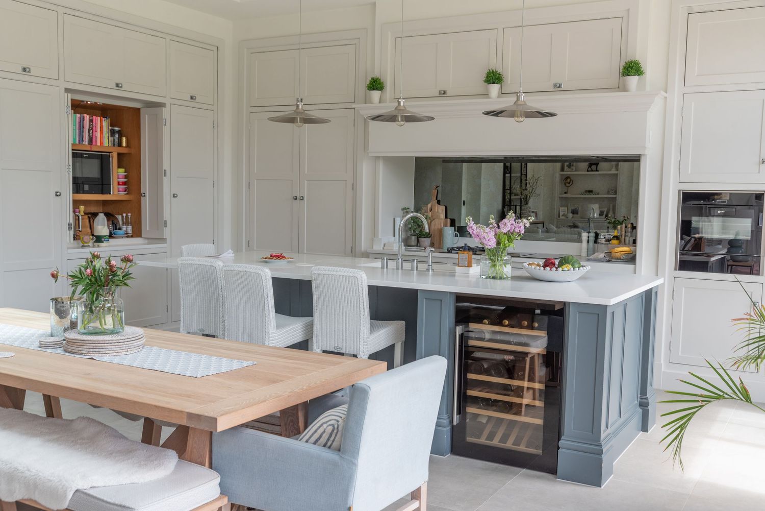 Elegant open-plan kitchen with grey island, wine cooler, white cabinetry, pendant lights, and dining area with upholstered chairs.