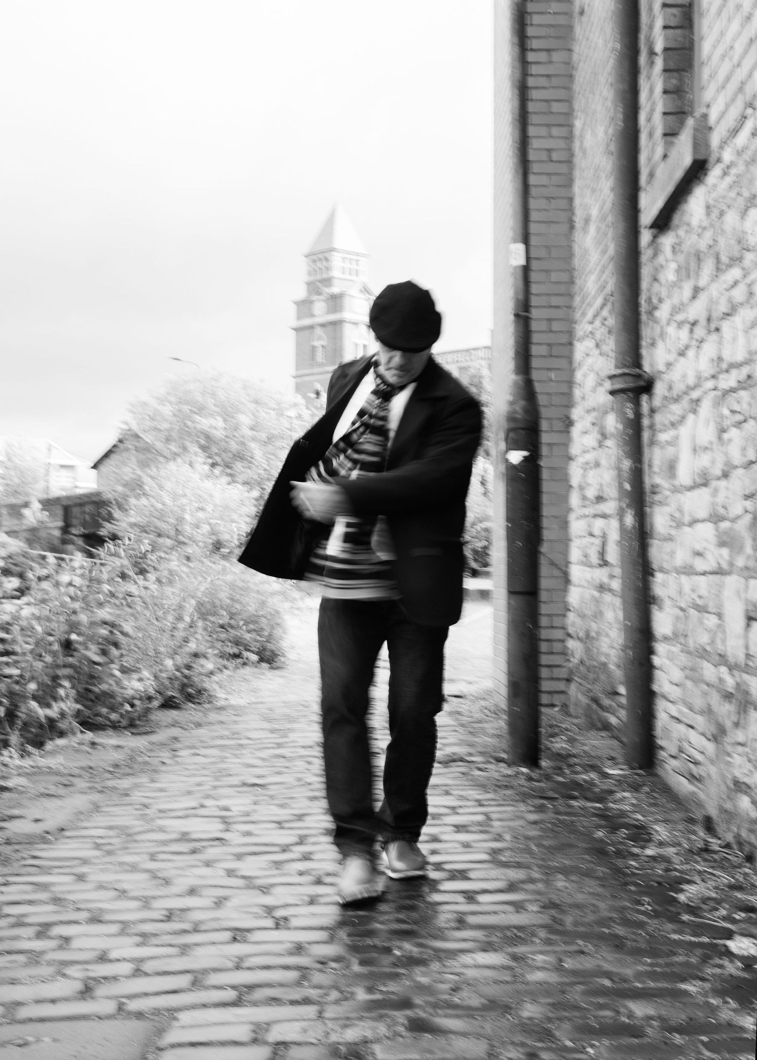 A sequence of black and white photos showing a person crouched down on a cobblestone path near a brick wall.