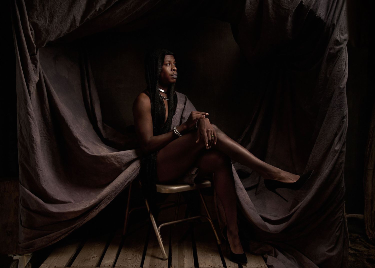 Atmospheric studio portrait with moody lighting and dark fabric backdrop creating dramatic shadows.