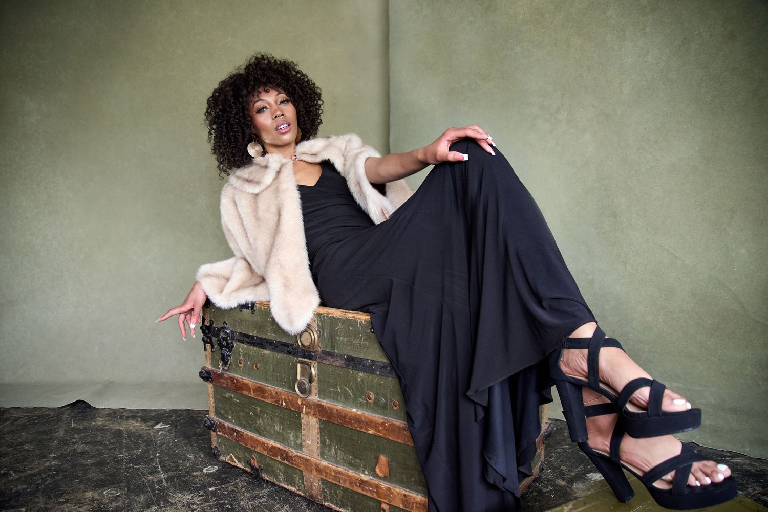 Artistic fashion shot of model sitting on vintage trunk with flowing garments.