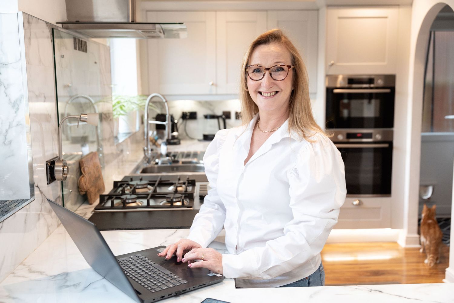 Person working on laptop in modern white kitchen with stainless appliances.