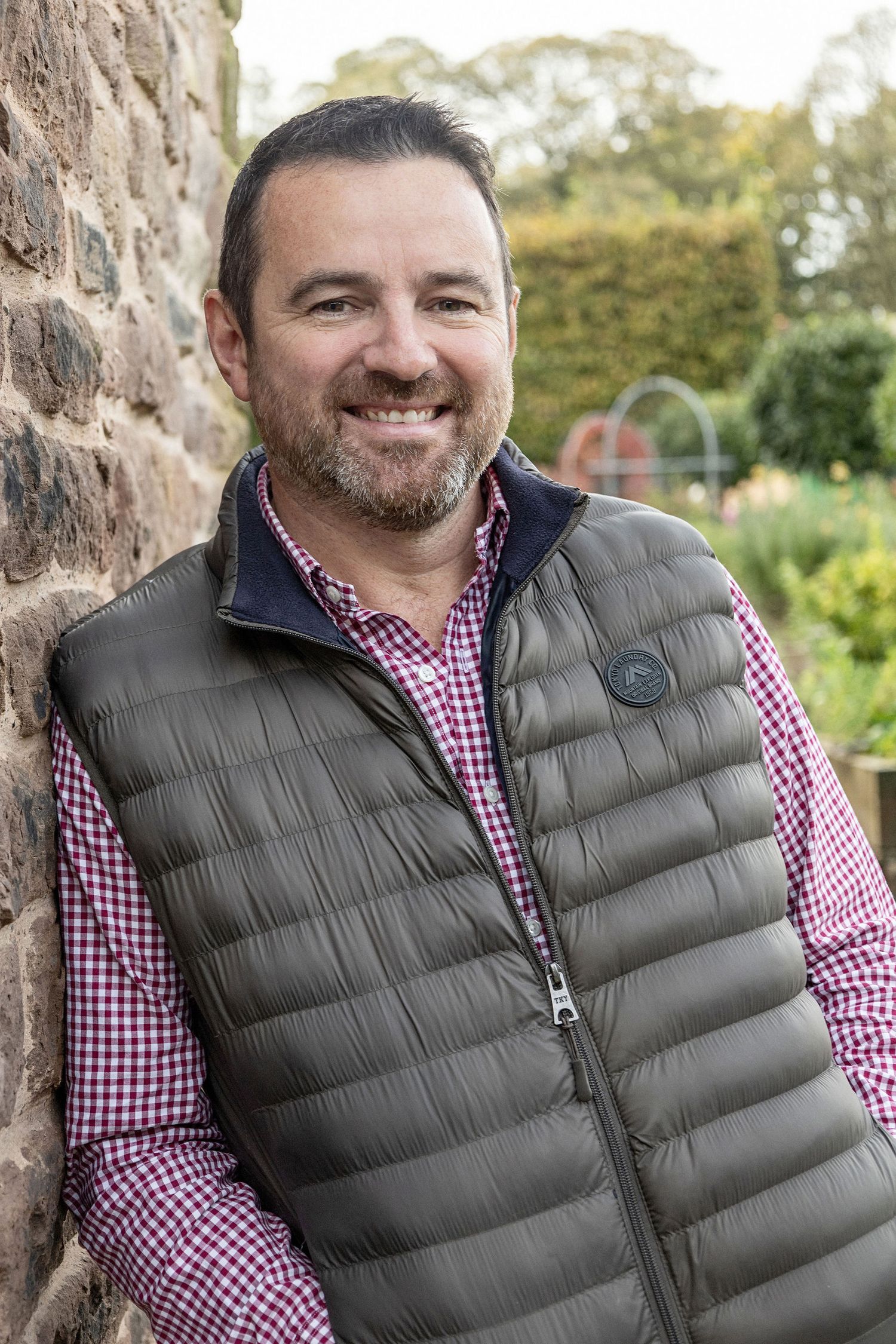 Outdoor portrait of person in gray puffy vest and checkered shirt against brick wall.