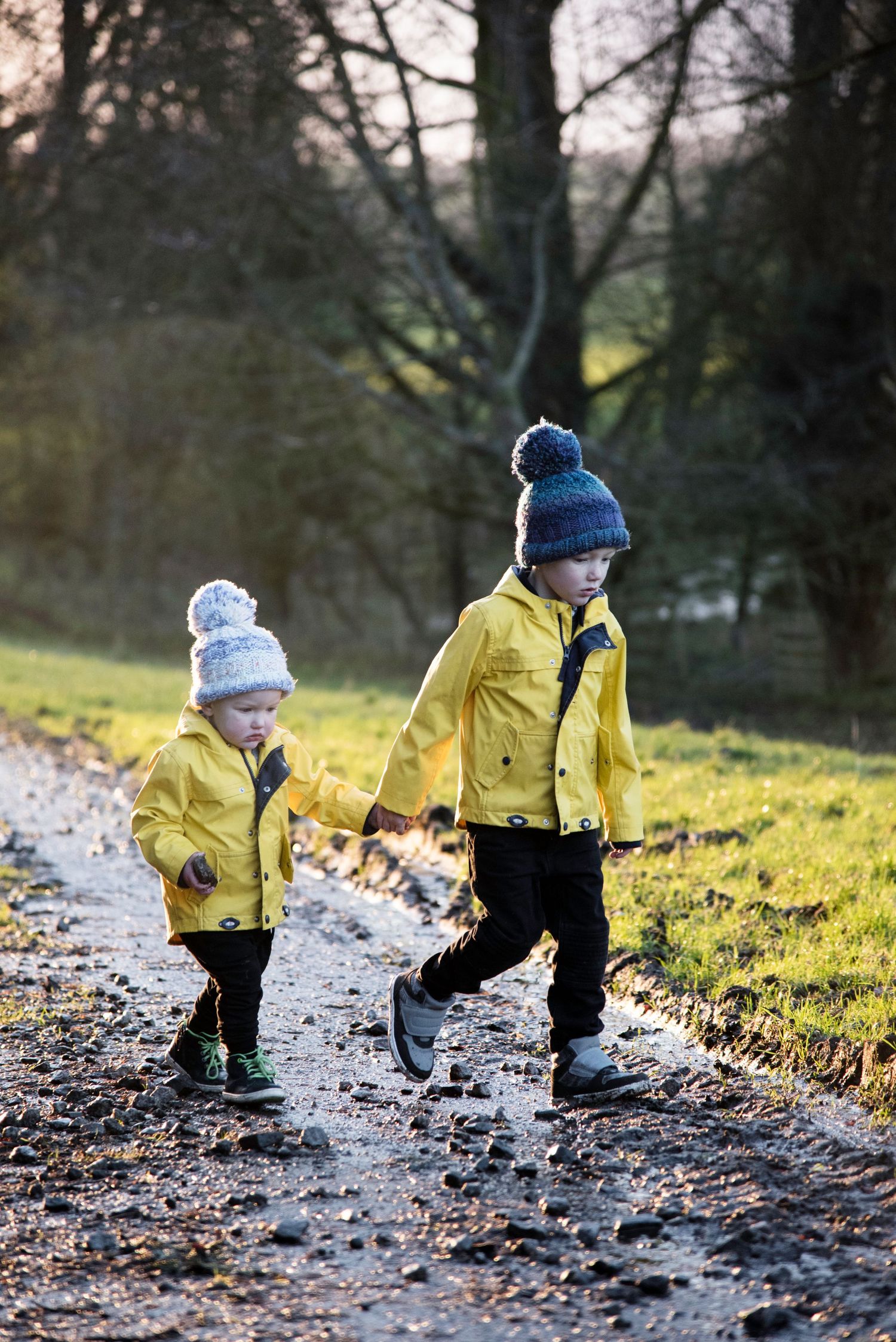 Small child wearing yellow raincoat and winter hat explores snowy ground in winter woodland setting.