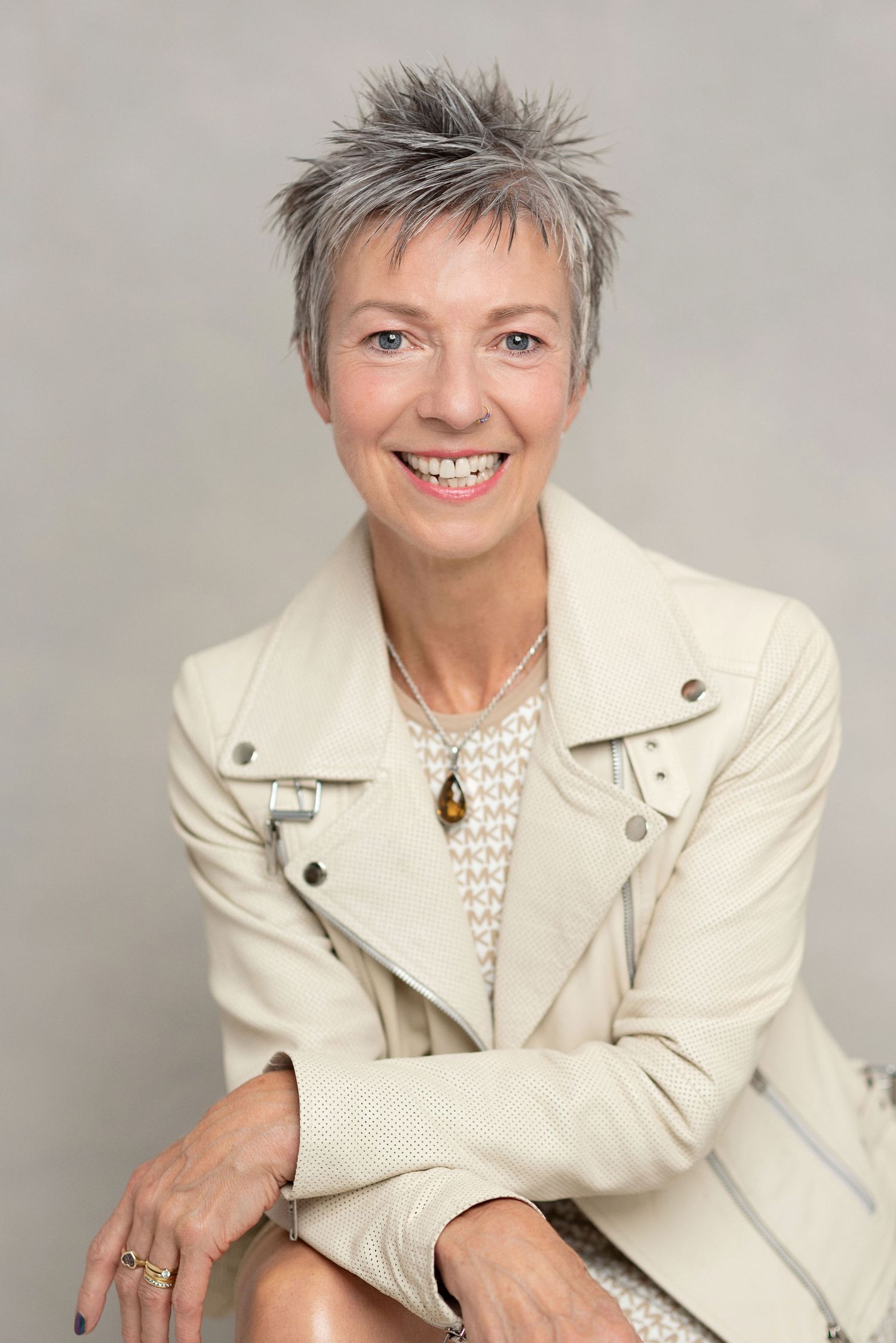 Stylish portrait in cream leather jacket and pearl necklace against neutral backdrop.