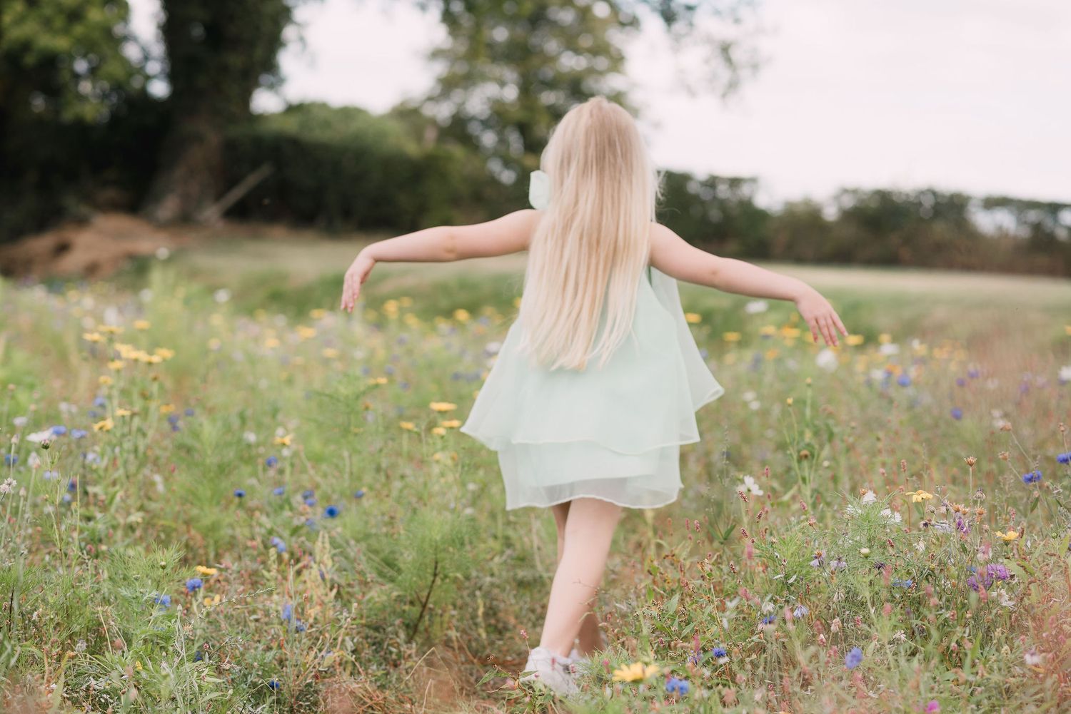 Person walking through a vibrant wildflower meadow on a sunny summer day wearing a flowing mint dress.