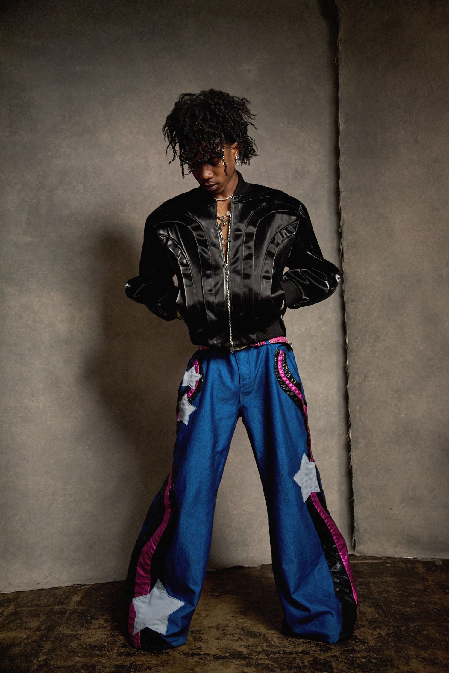 Fashion model in black jacket and decorated blue jeans posing against gray background.