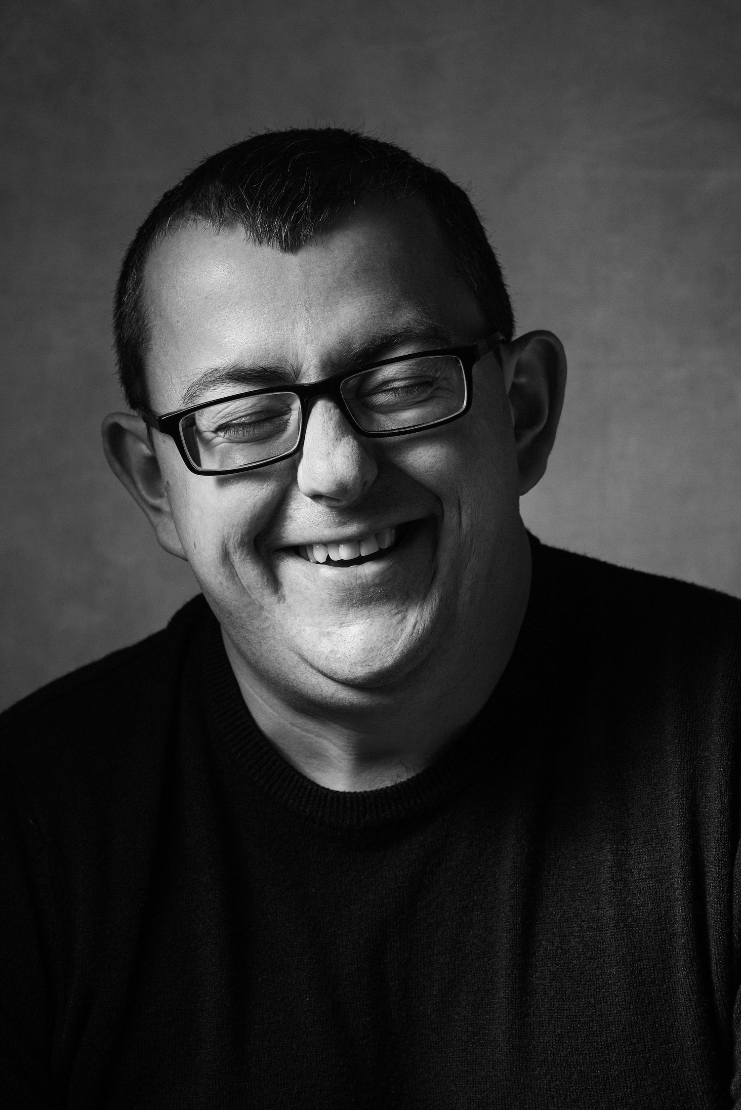 A black and white portrait series showing a person wearing glasses with different smiling expressions.