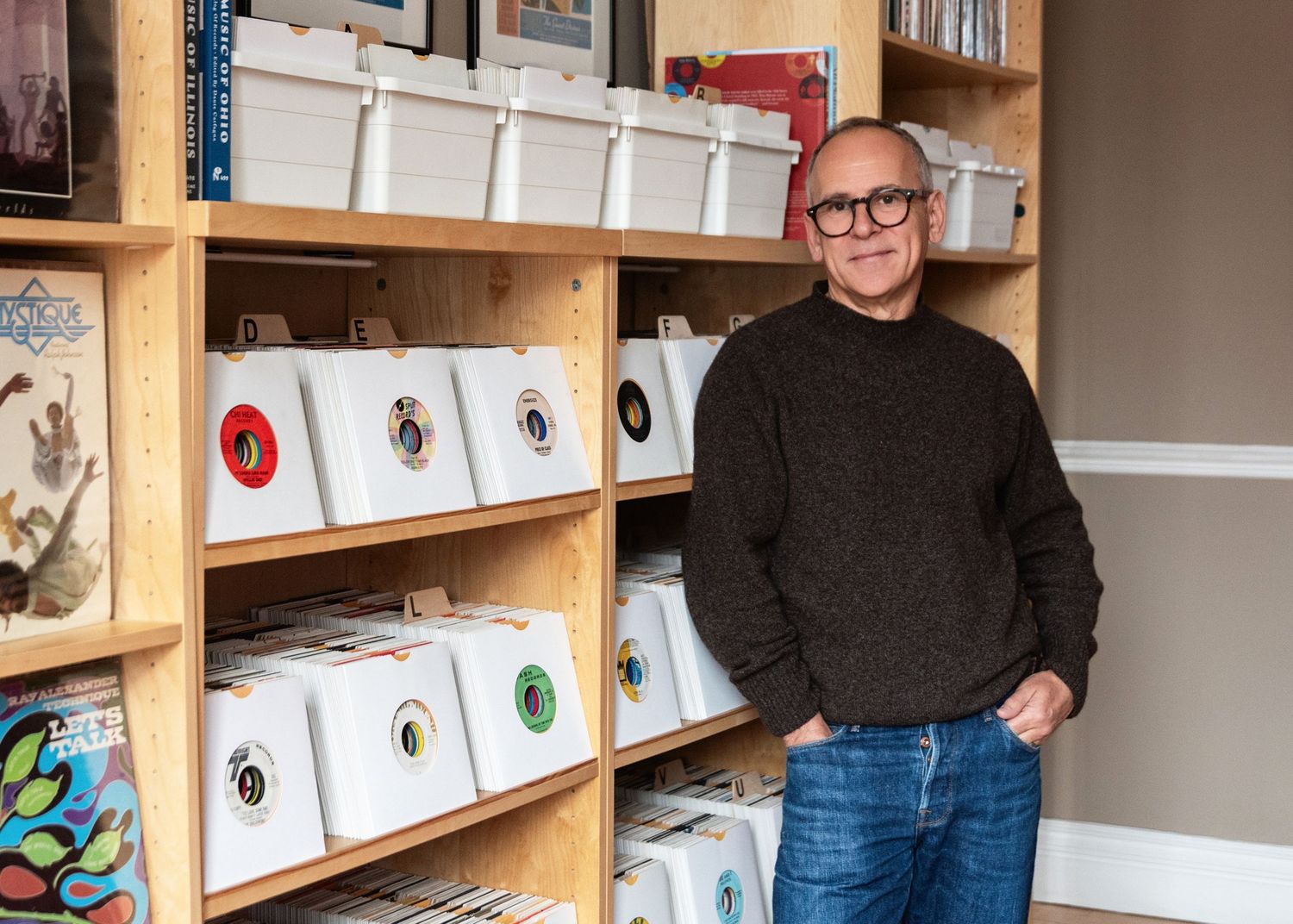 Someone stands in front of wooden shelves displaying vinyl records and music merchandise in a retail shop.
