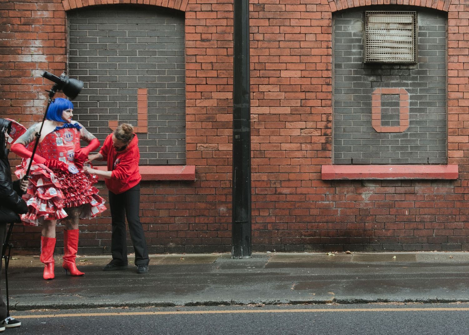 Two people in vibrant red costumes stand outside a brick building on a wet street.