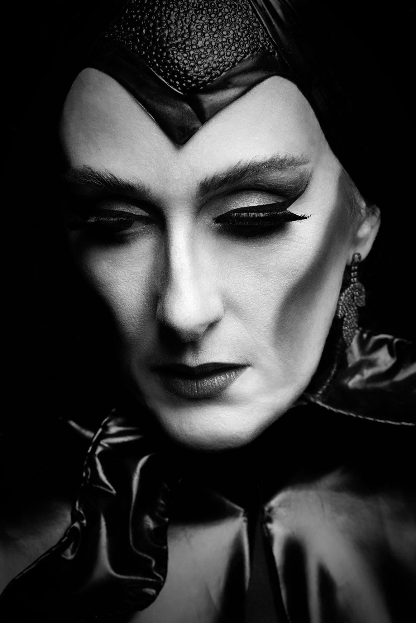 Dramatic black and white portrait showing glamorous dark makeup and headpiece styling.