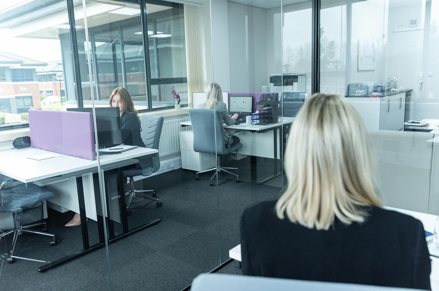 Modern office space with multiple workstations and professionals at their desks.
