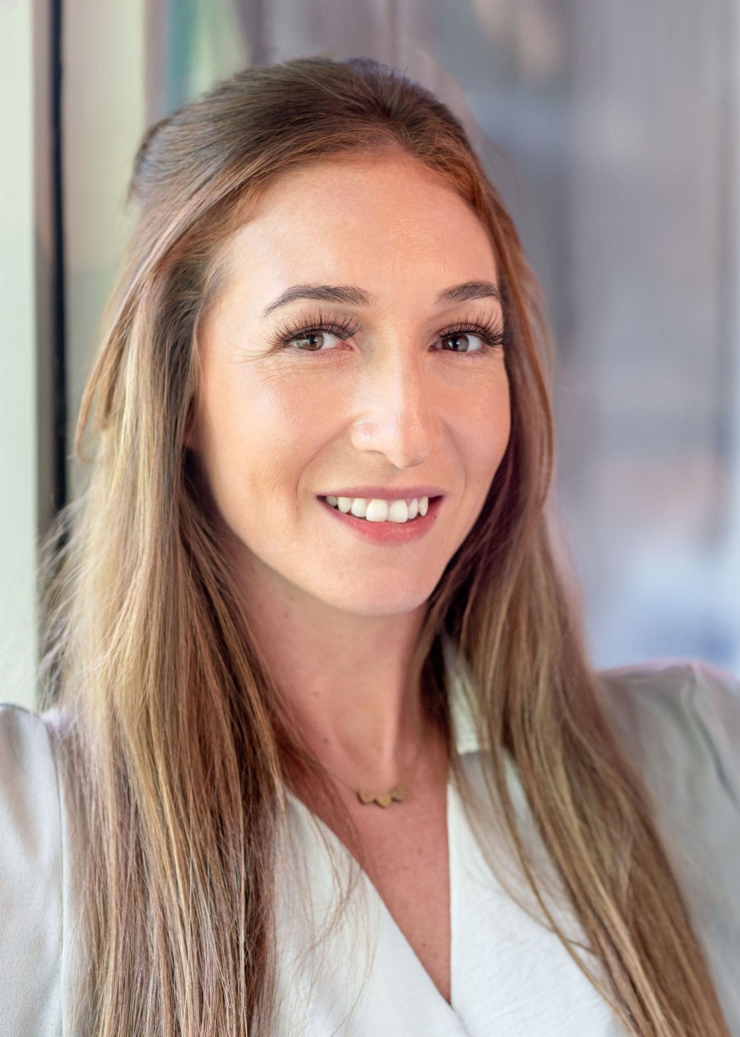 Professional portrait of woman in white blouse with long hair against office background.