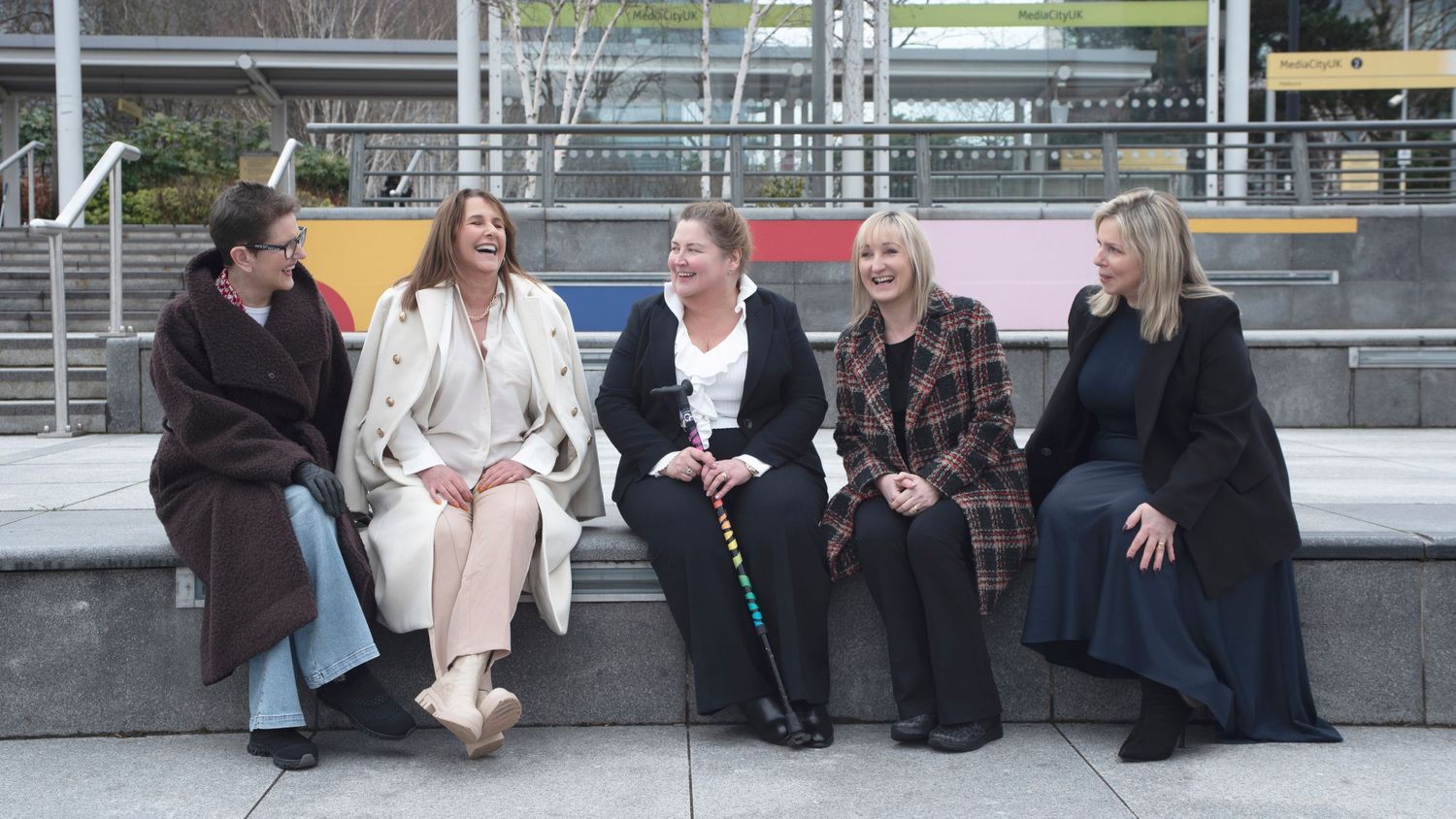 Five team members sitting together on concrete steps outside a building in casual conversation.