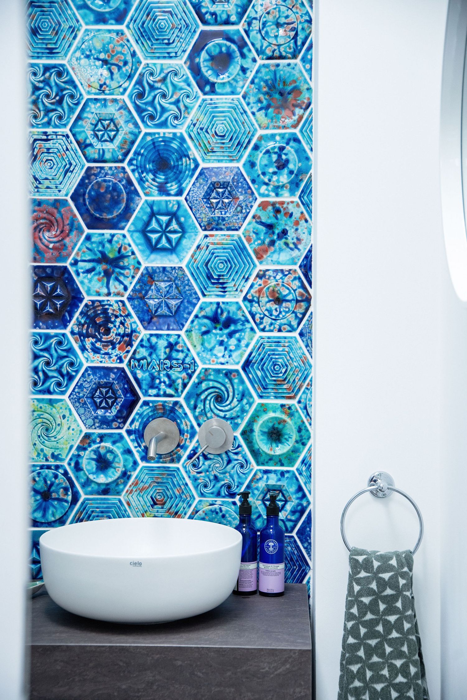 Modern bathroom with vibrant blue hexagonal mosaic tile backsplash and white vessel sink on dark countertop.