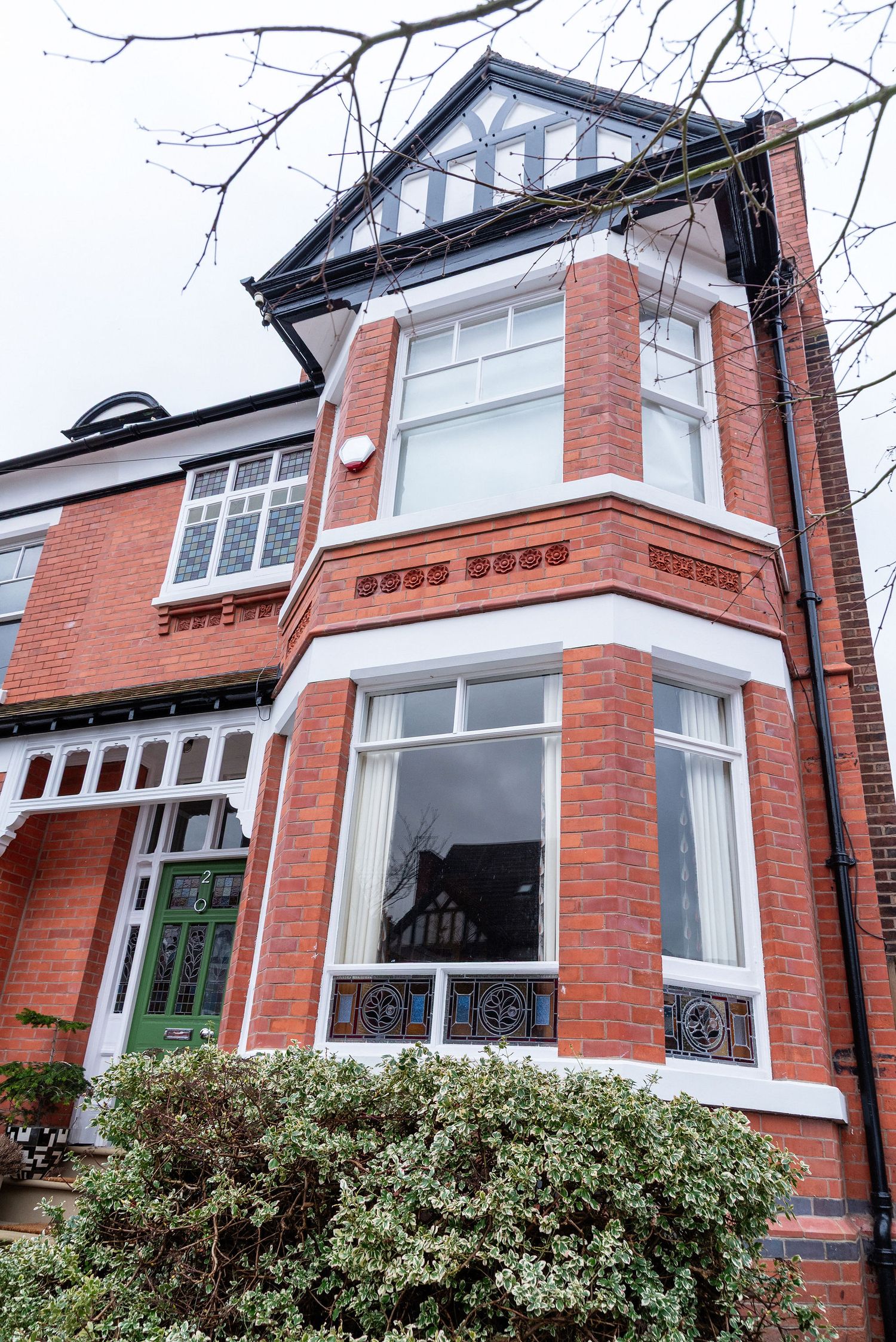 Traditional red brick Victorian townhouse with bay windows, ornate details and gabled roof in a residential neighborhood.