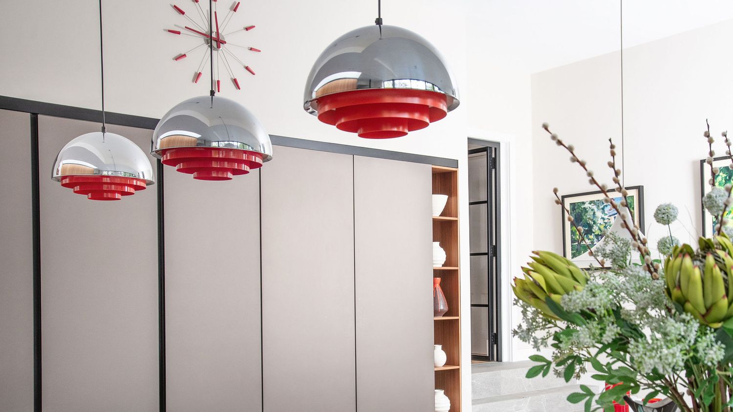 Modern office space with red pendant lamps, white walls, and indoor plants creating a bright, contemporary workspace.