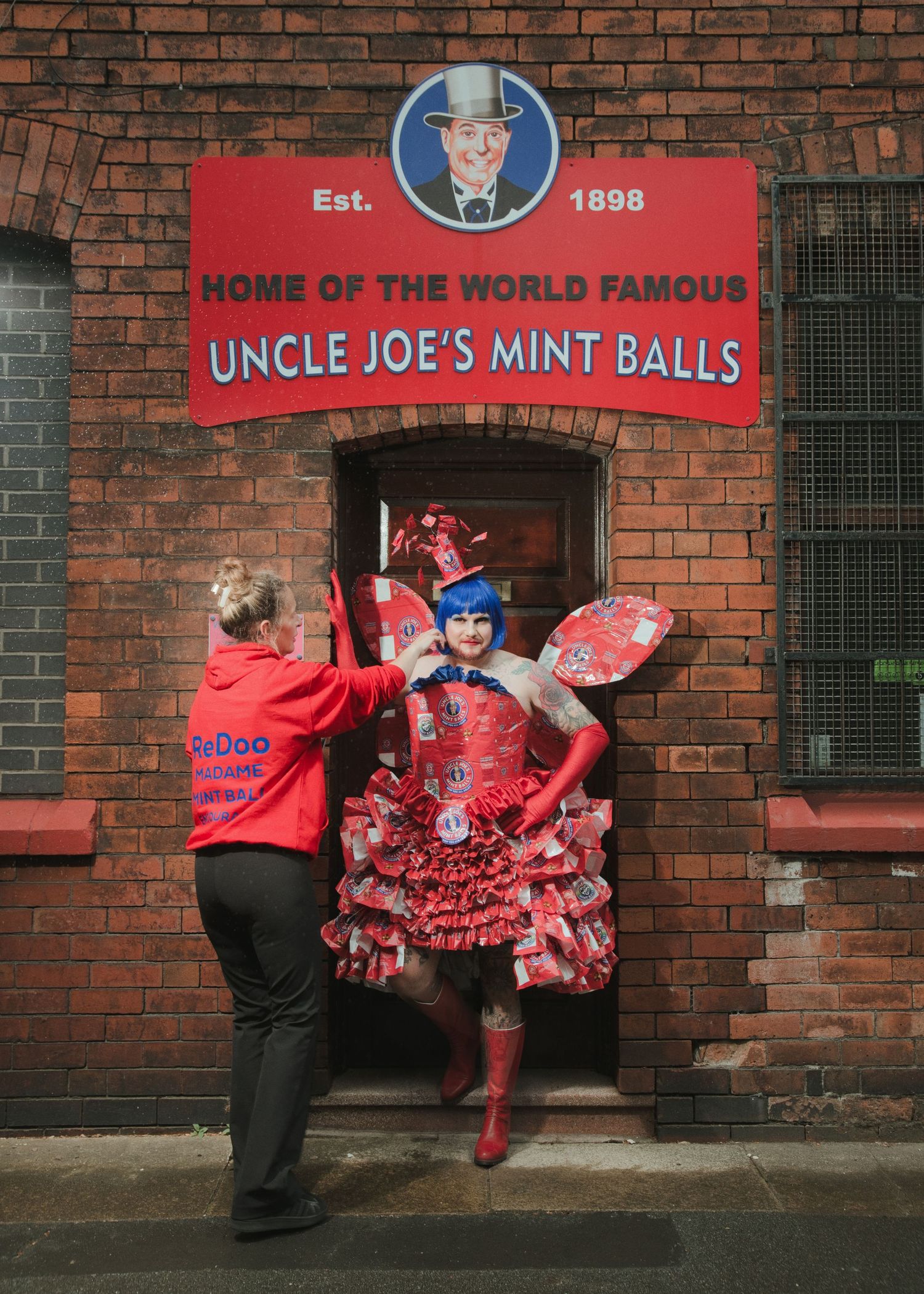 Person in elaborate red costume outside Uncle Joe's Mint Balls shop, established 1898, assisted by staff member.