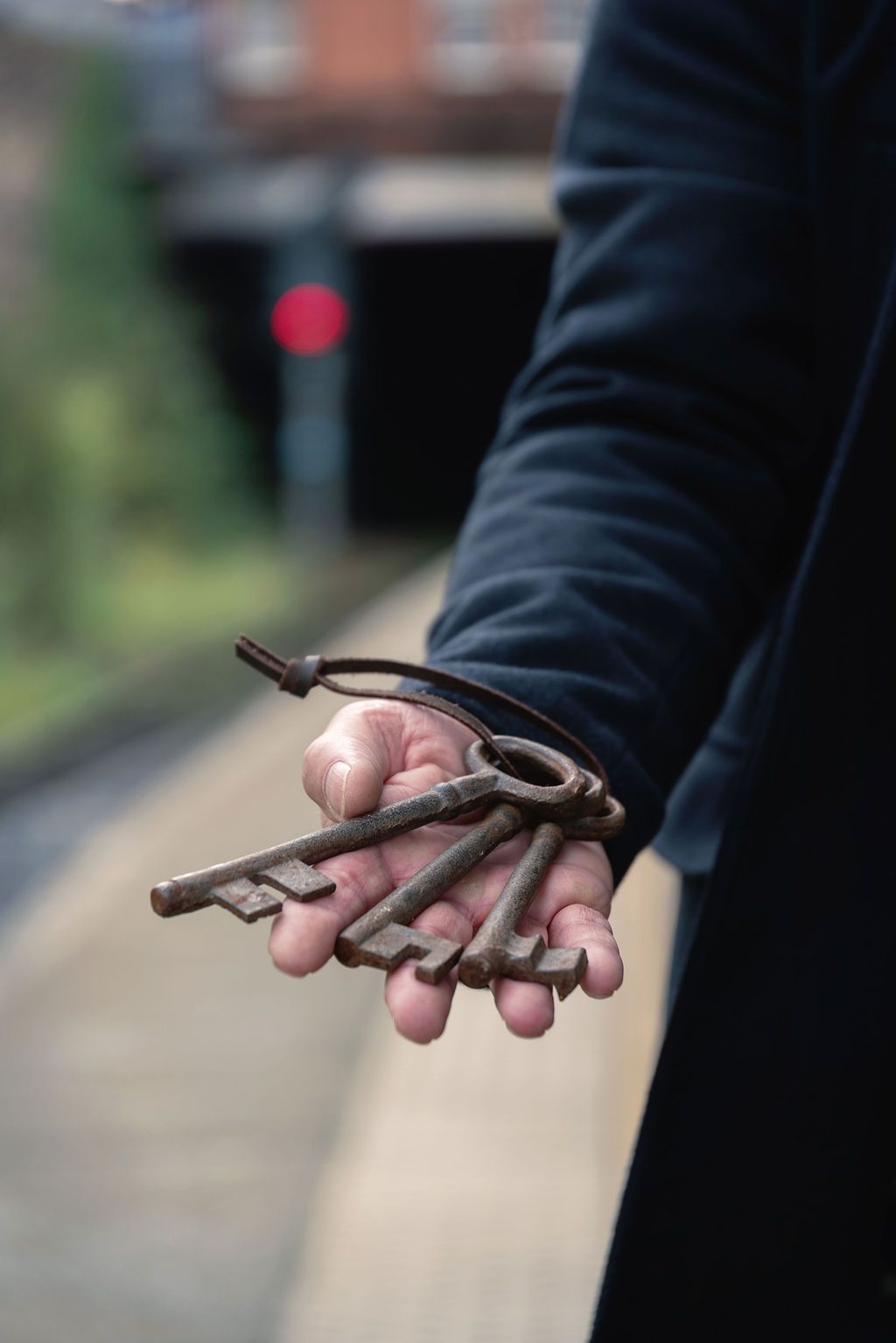 Hand holding a bundle of antique rusty skeleton keys on a ring at a train station.