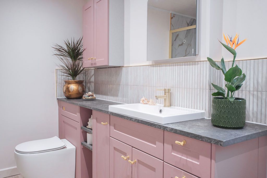 Modern pink and white bathroom with gold accents featuring a freestanding tub and decorative plants.
