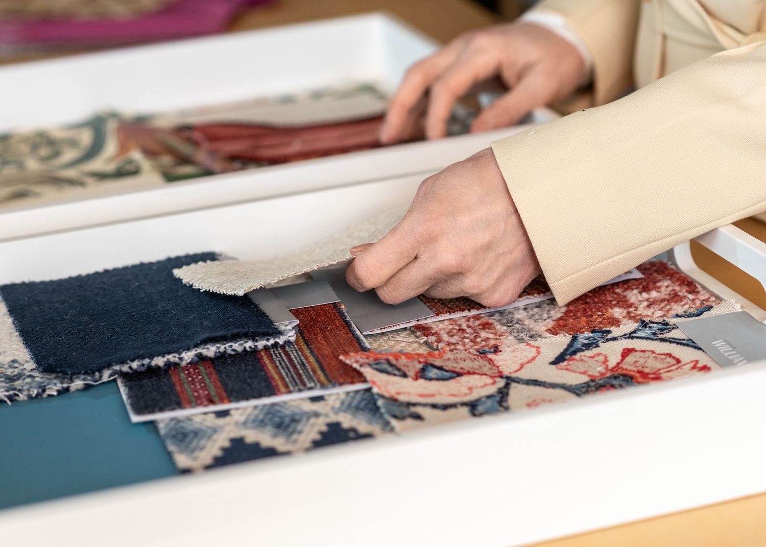 Close-up view of hands arranging fabric swatches and patterns for a design project on a white surface.