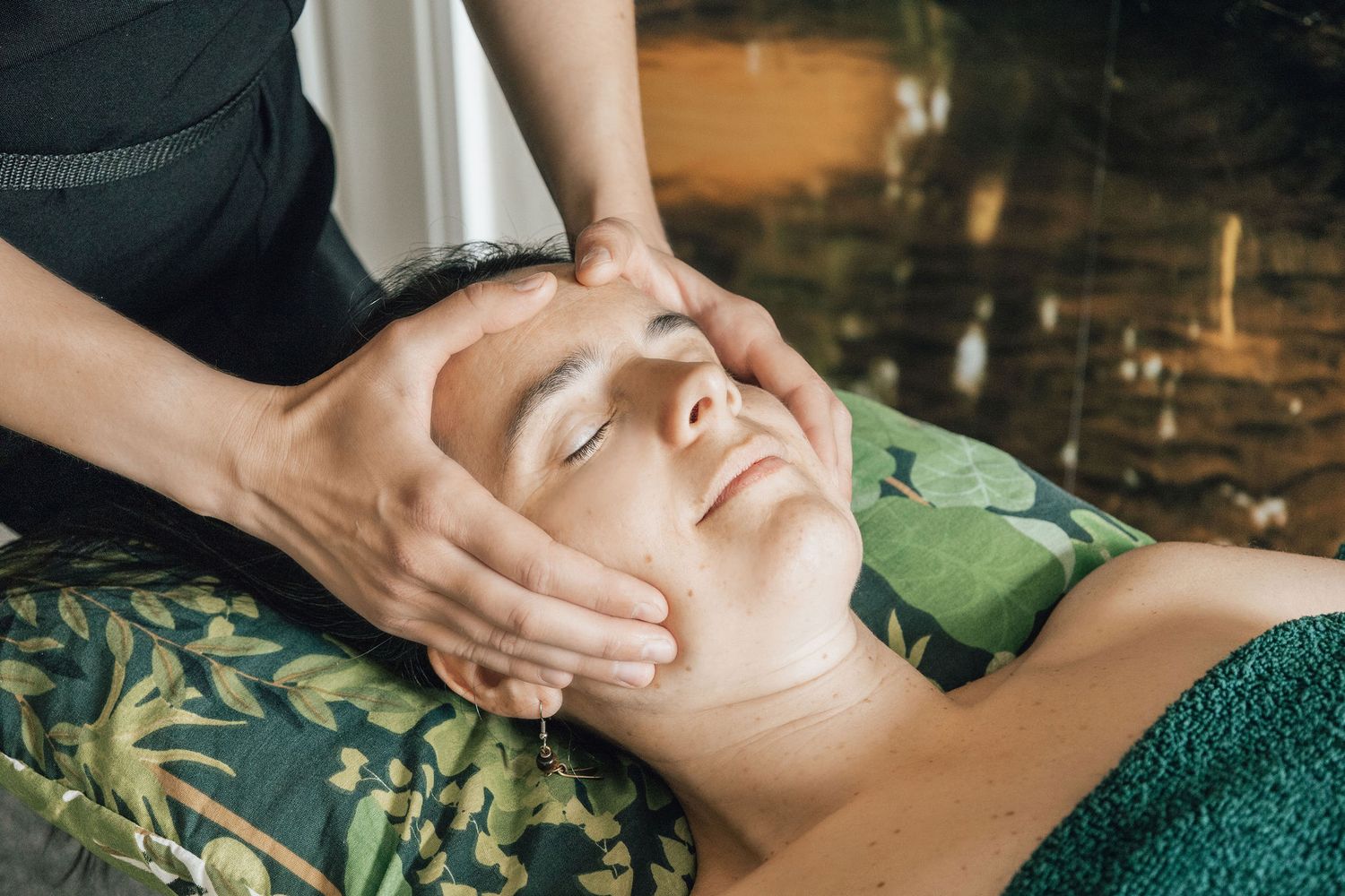 A person receiving a facial massage treatment while lying on a green towel.