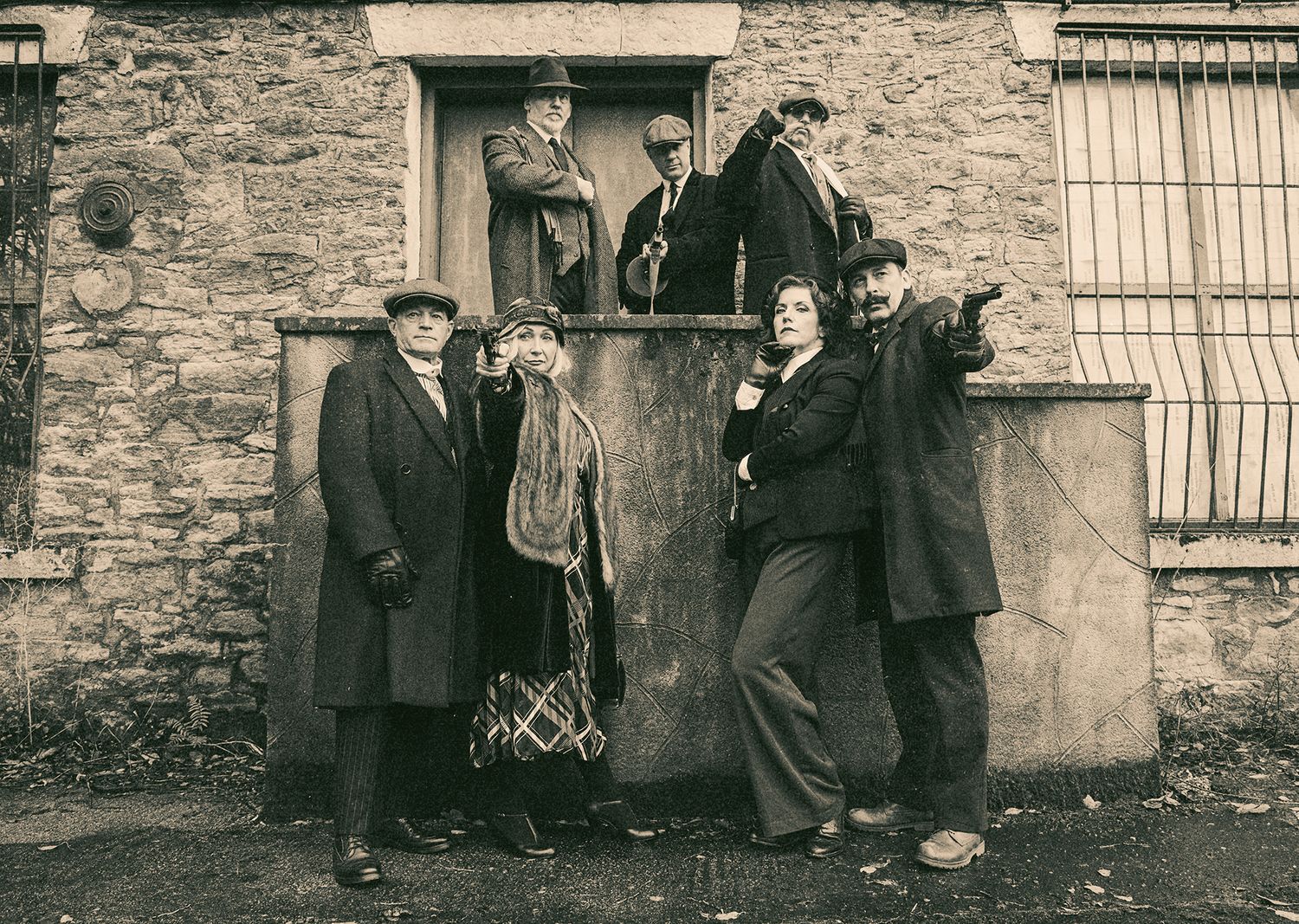 Group in vintage 1920s clothing poses playfully outside stone building entrance.