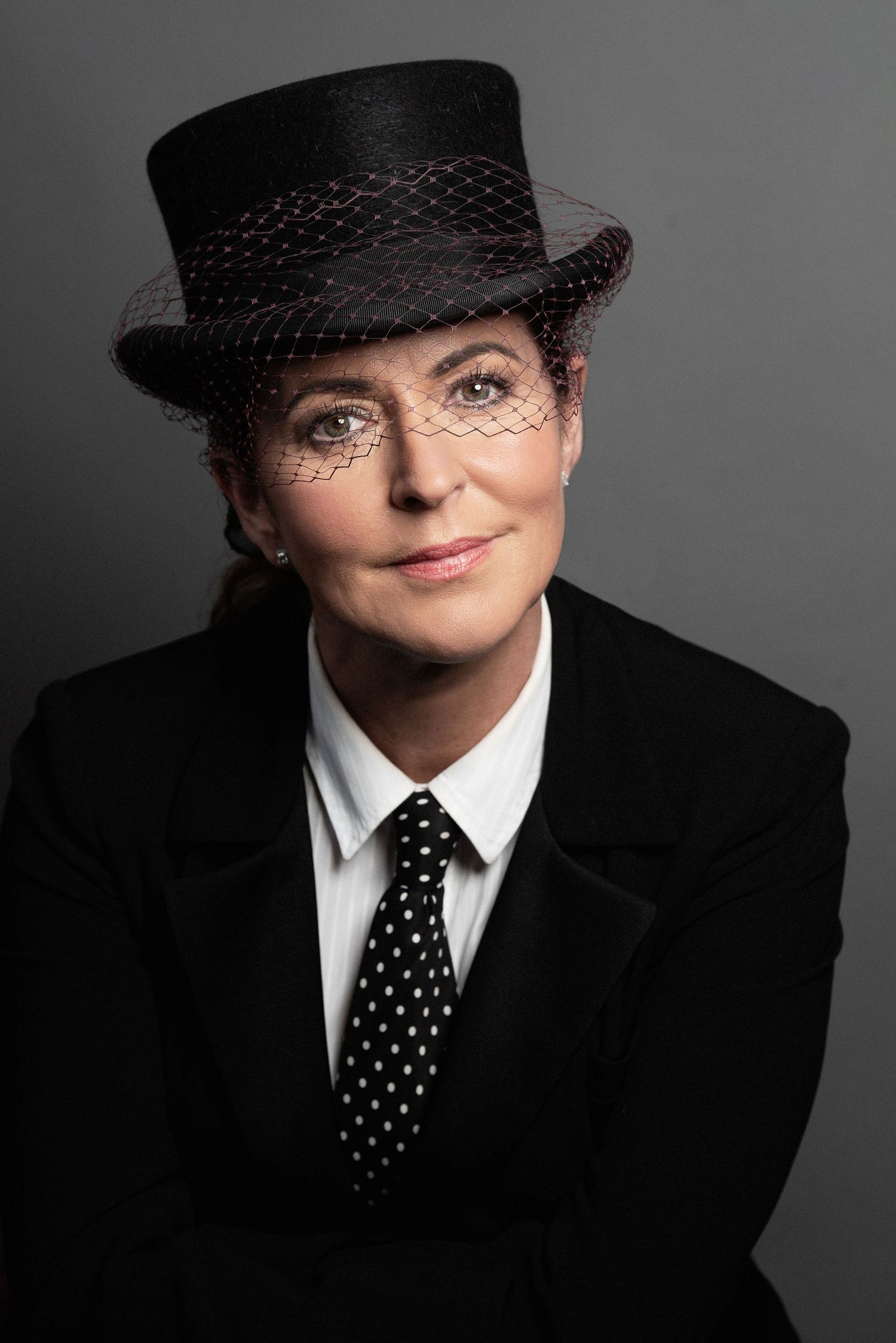 Studio portrait featuring black top hat with veil, polka dot tie and formal attire.