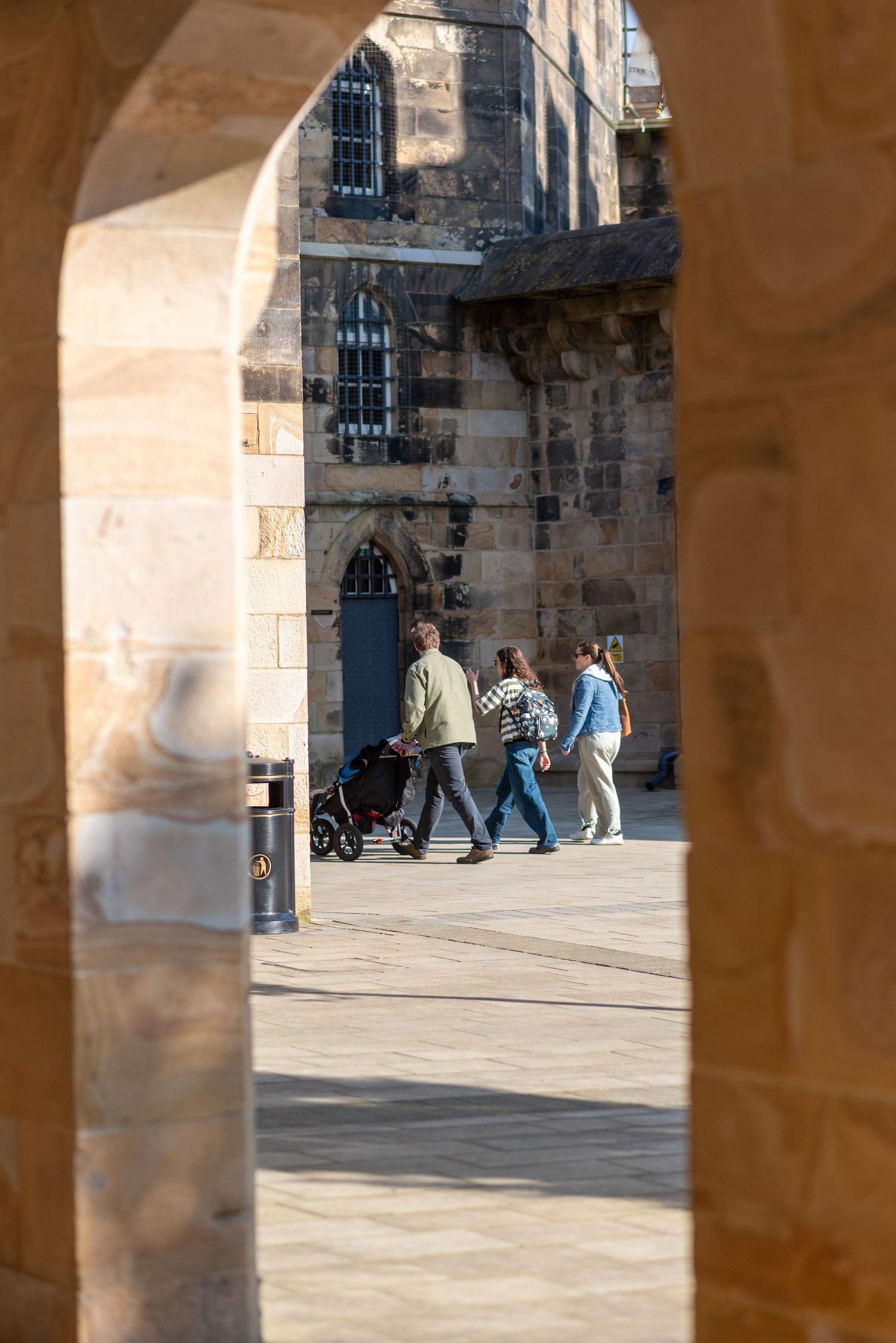 Stone archway framing view of people walking past historic building with blue doors.