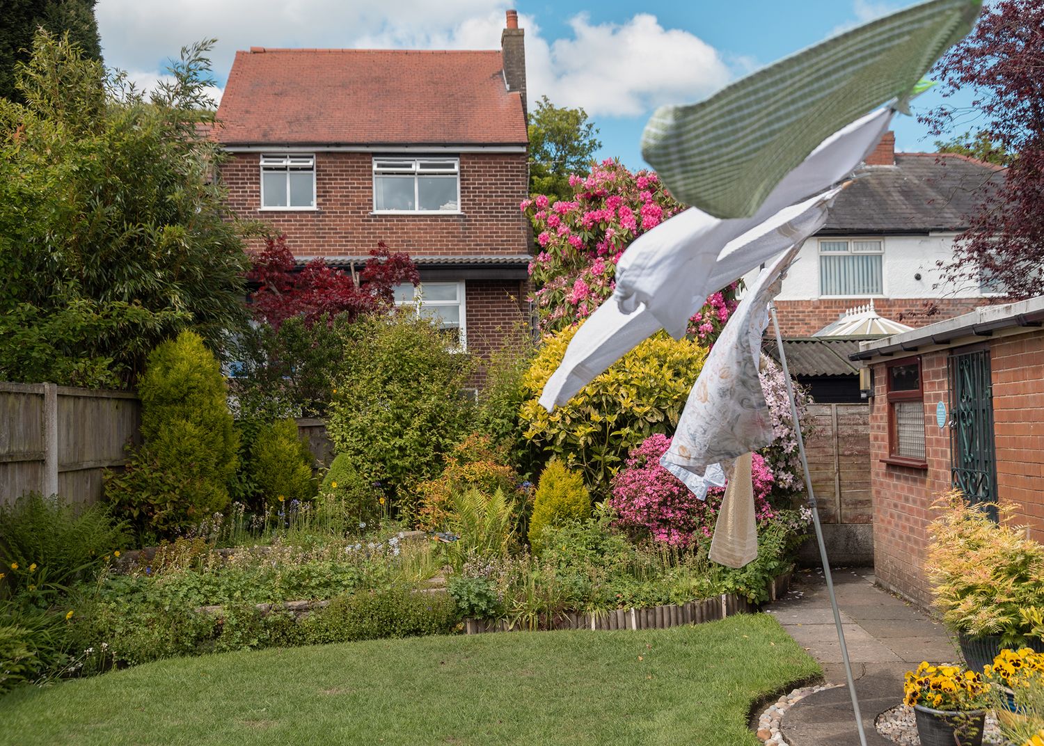 Large white bird sculpture soaring above a colorful English garden with brick houses and lush flowering shrubs.