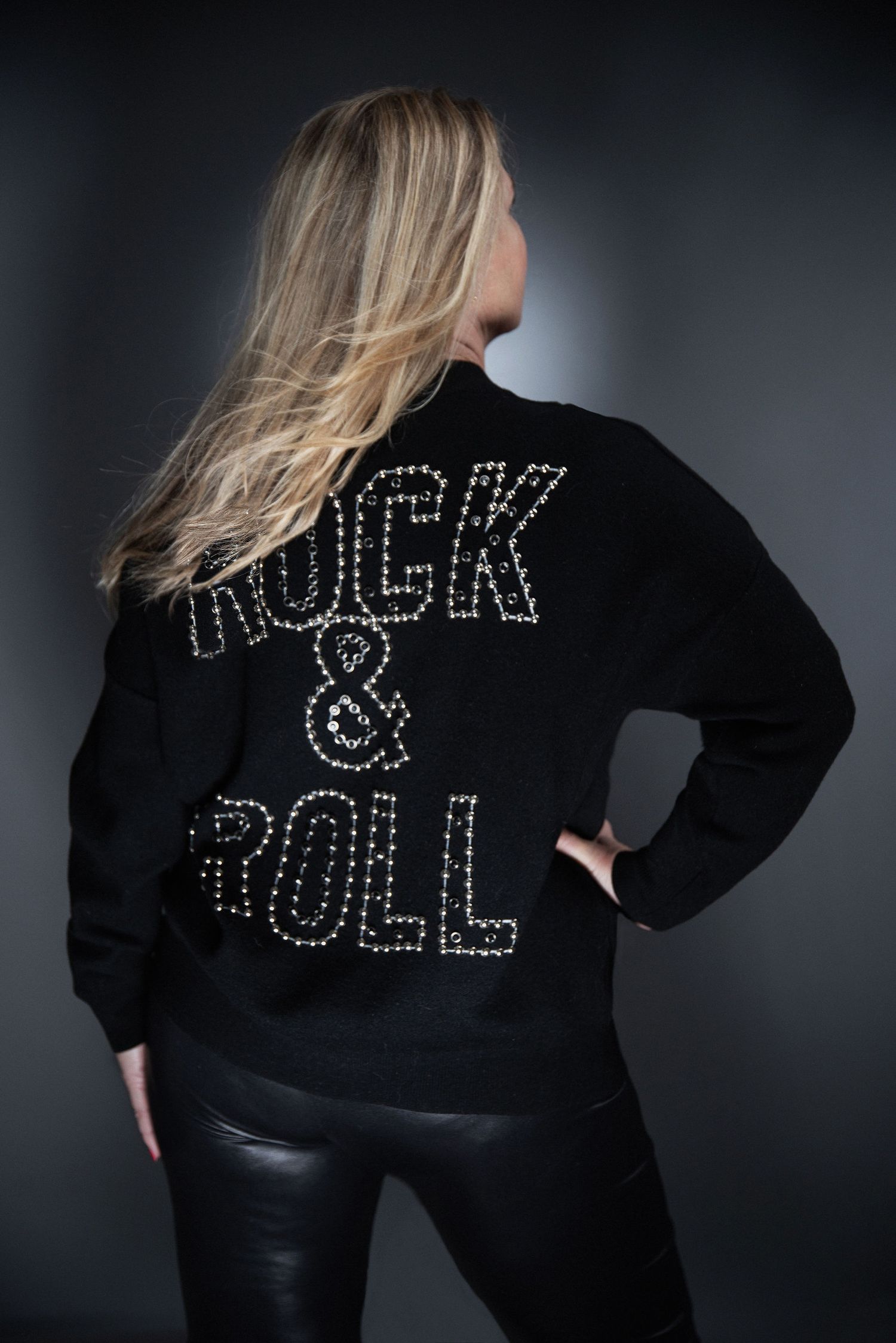 A black sweatshirt with studded 'ROCK & ROLL' text on the back worn against a dark background.